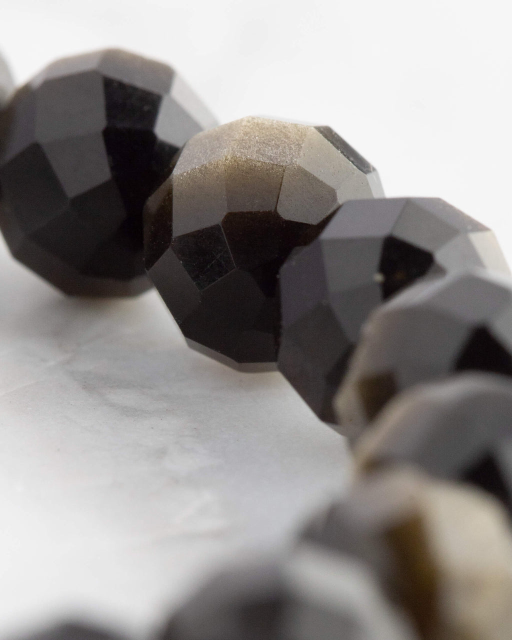 Macro de una cuenta facetada de Obsidiana Dorada junto a otras de tono negro