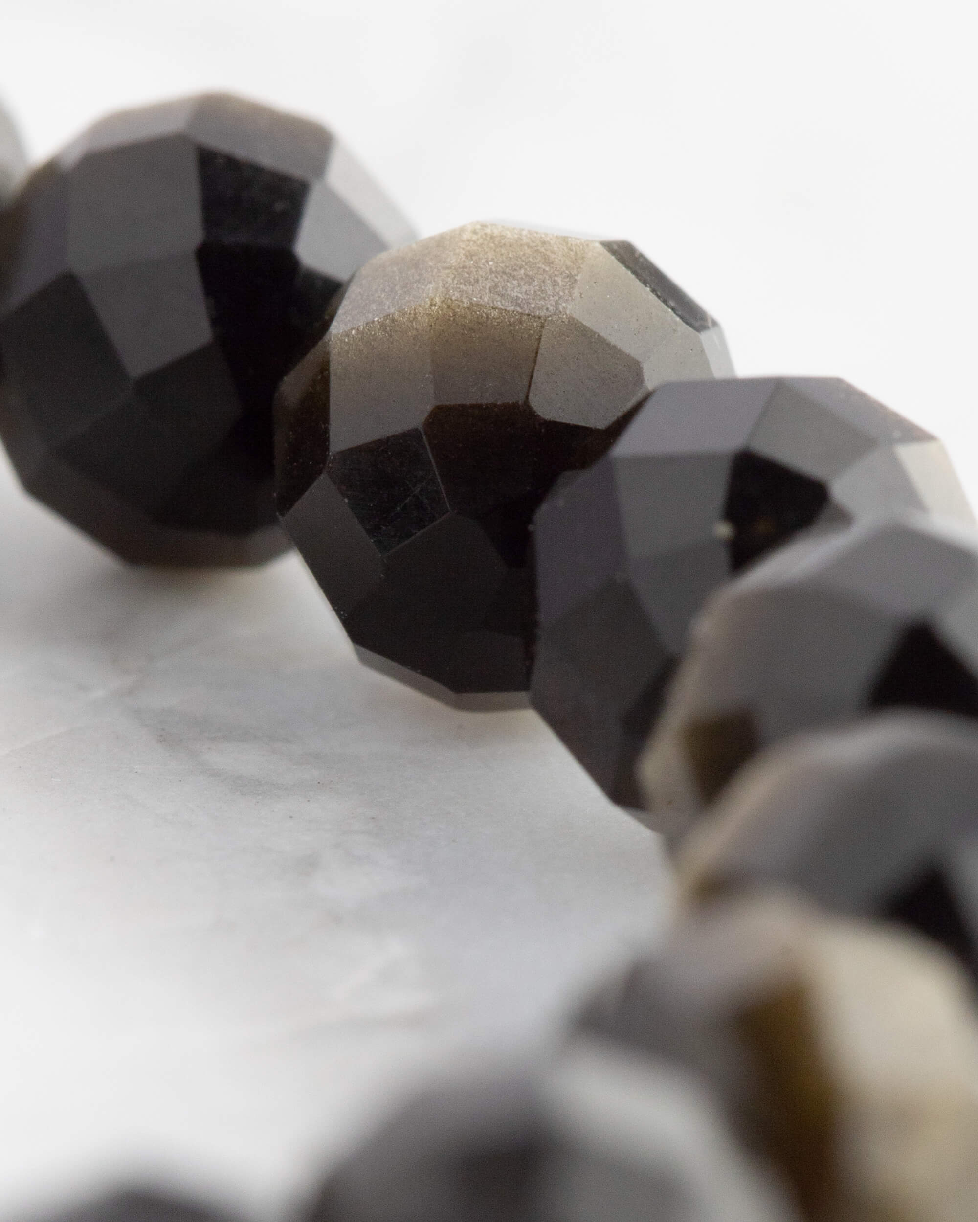 Macro de una cuenta facetada de Obsidiana Dorada junto a otras de tono negro