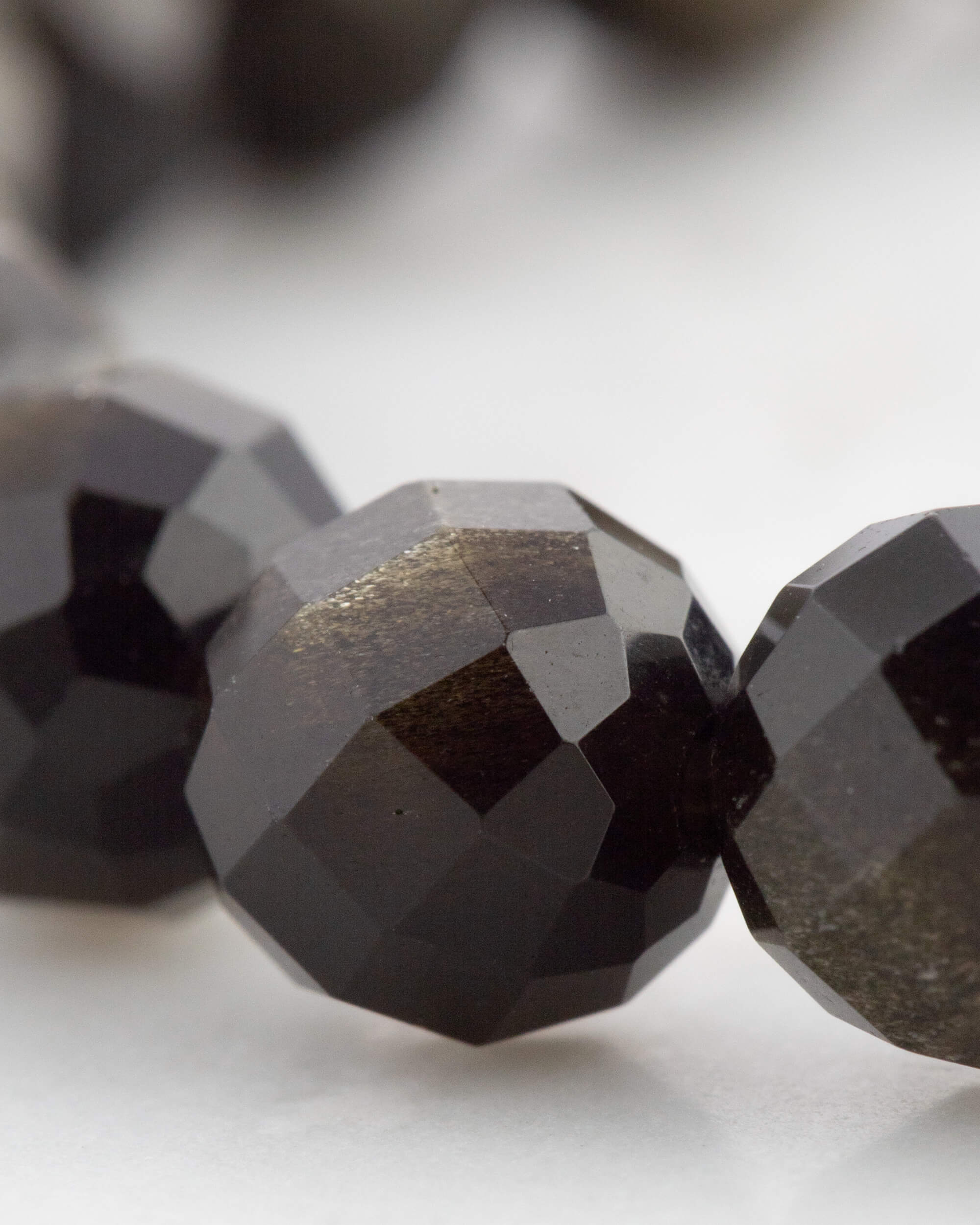 Detalle macro de las cuentas facetadas de Obsidiana Dorada con reflejo dorado
