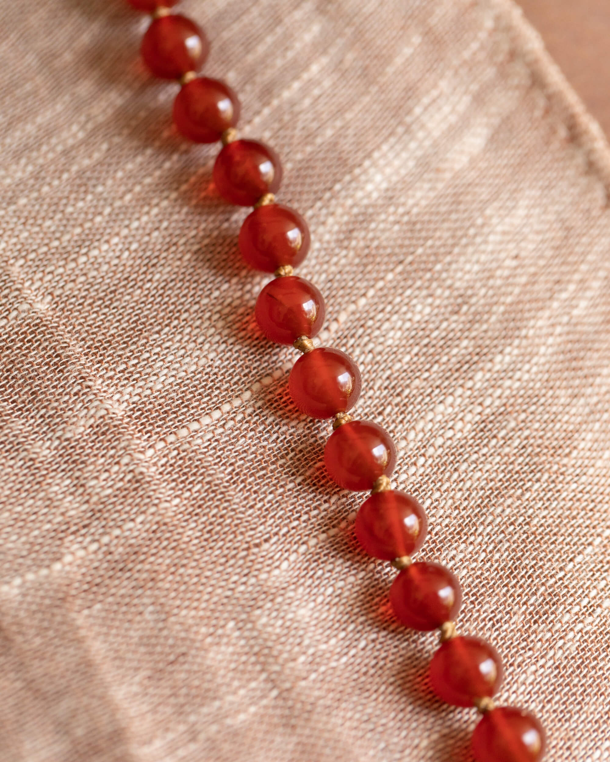 Japa mala de Cornalina en macro, hilera diagonal de cuentas brillantes sobre tela clara