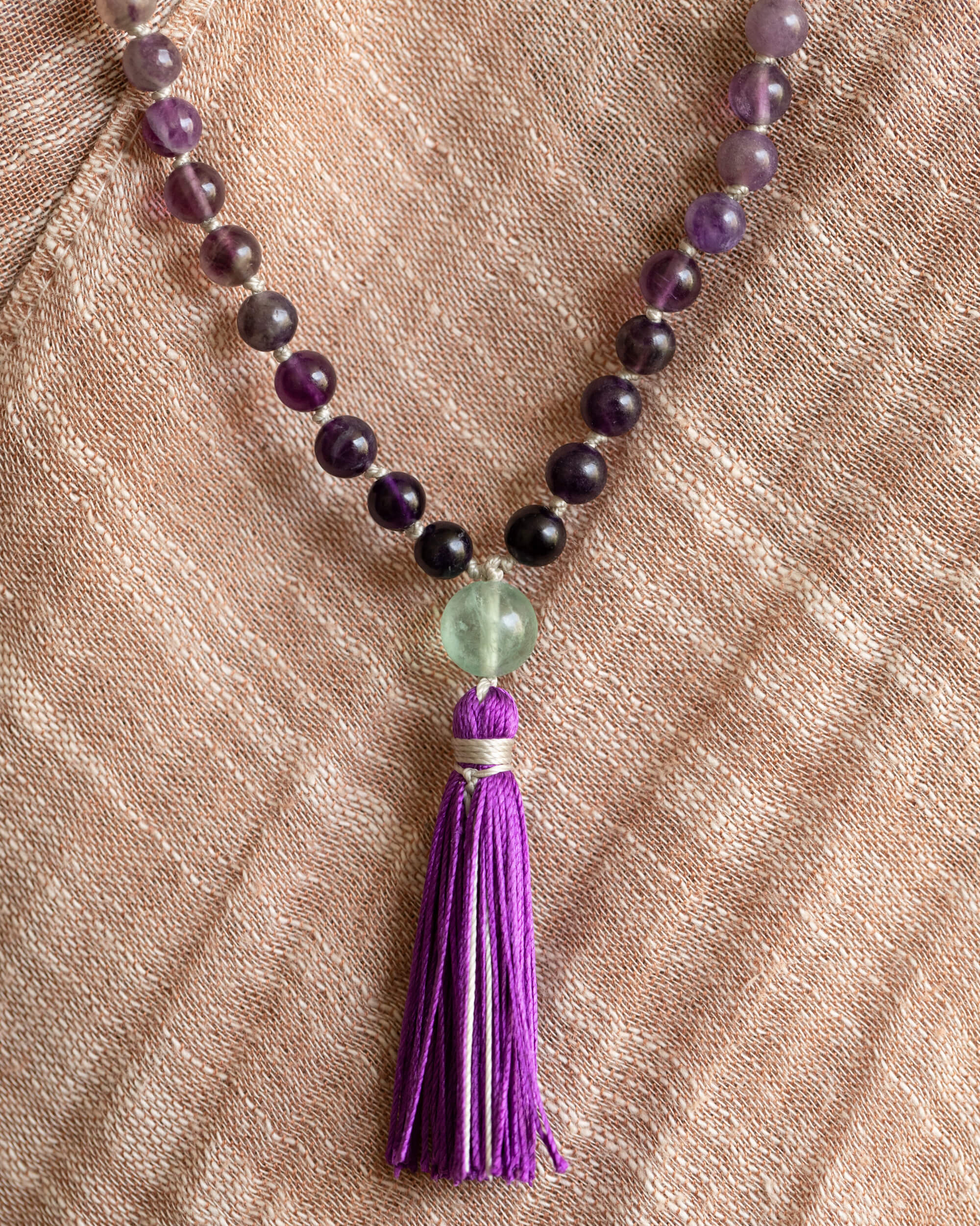 Japa Mala de Fluorita, vista cercana del guru bead verde y la borla morada sobre tela