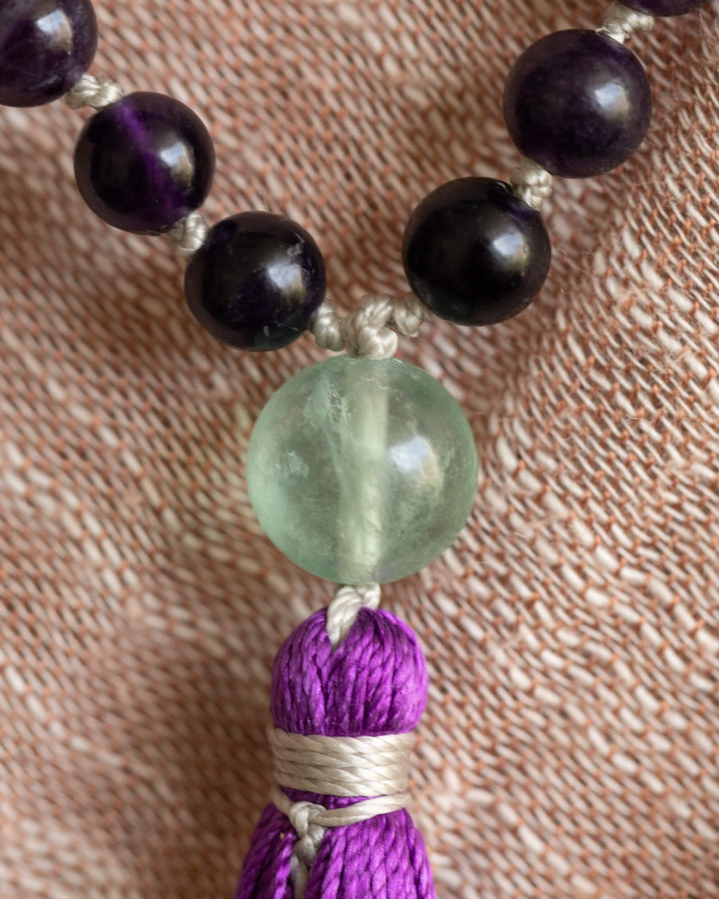Detalle macro del guru bead de Fluorita verde y la borla morada sobre tela