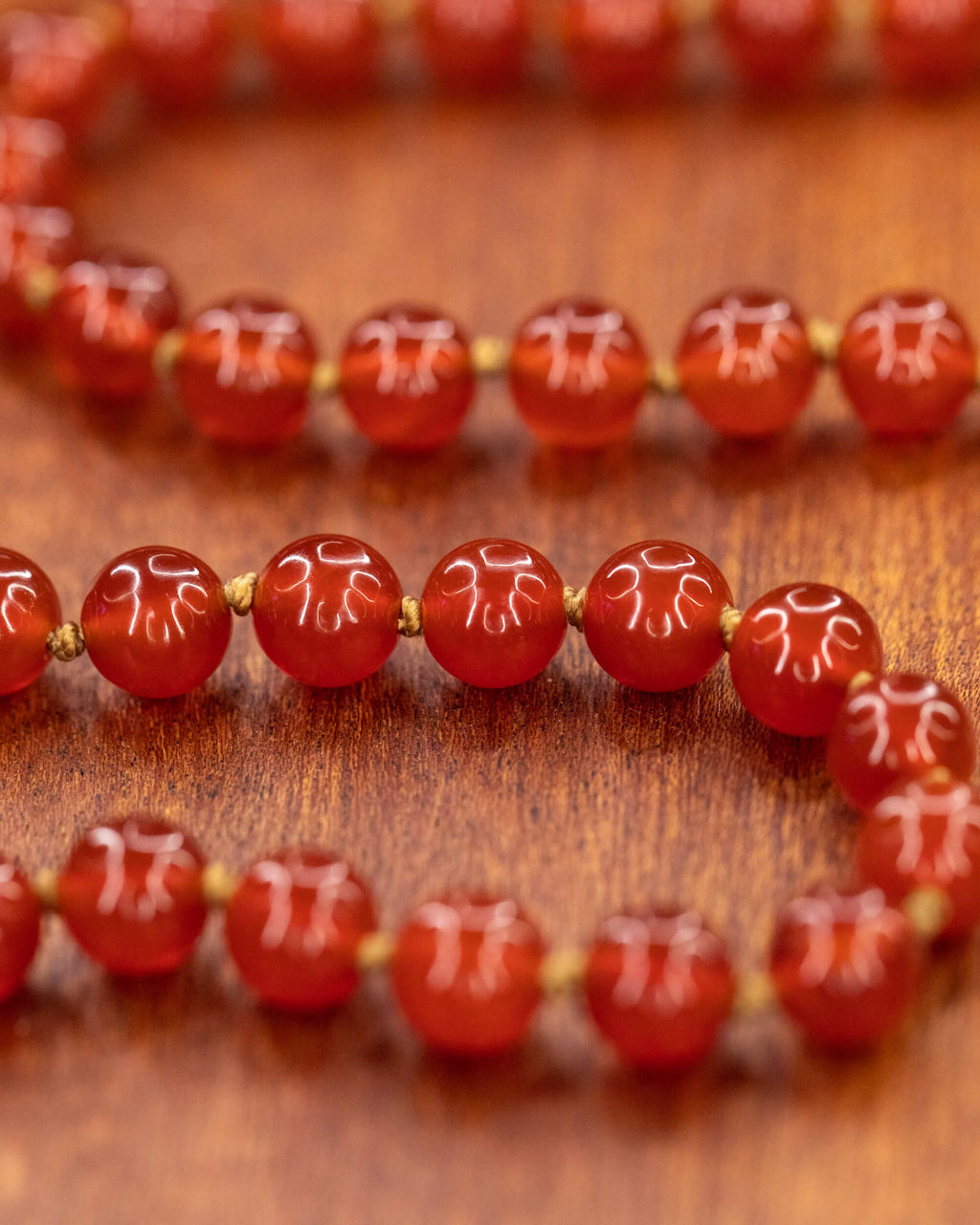 Japa mala de Cornalina en macro, cuentas rojas con grabado floral blanco sobre madera