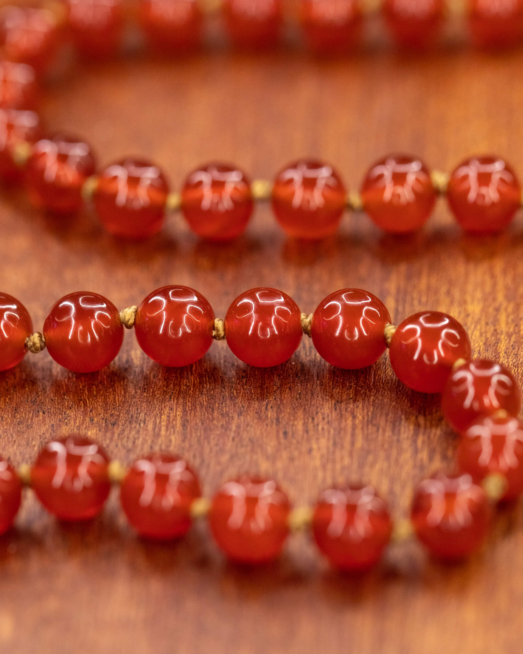 Japa mala de Cornalina en macro, cuentas rojas con grabado floral blanco sobre madera