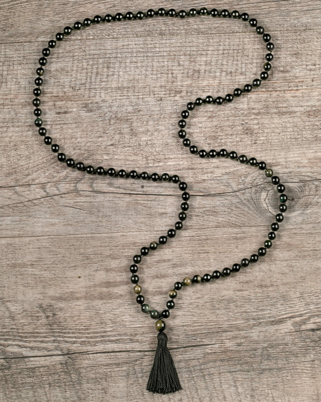 Japa Mala de Obsidiana Dorada extendido en forma de S sobre madera clara