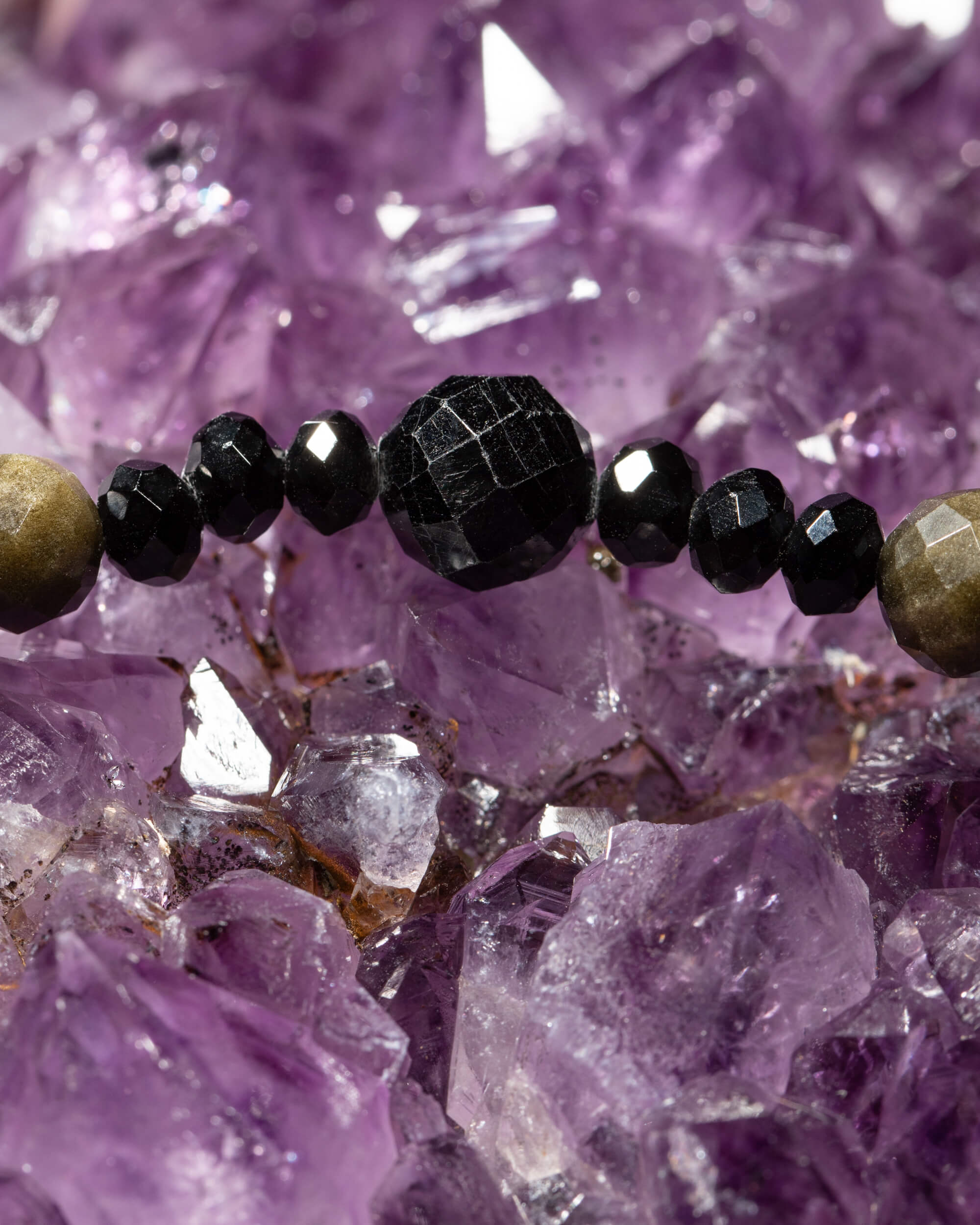 Detalle macro de las cuentas facetadas de Turmalina Negra y Obsidiana Dorada sobre druza de amatista