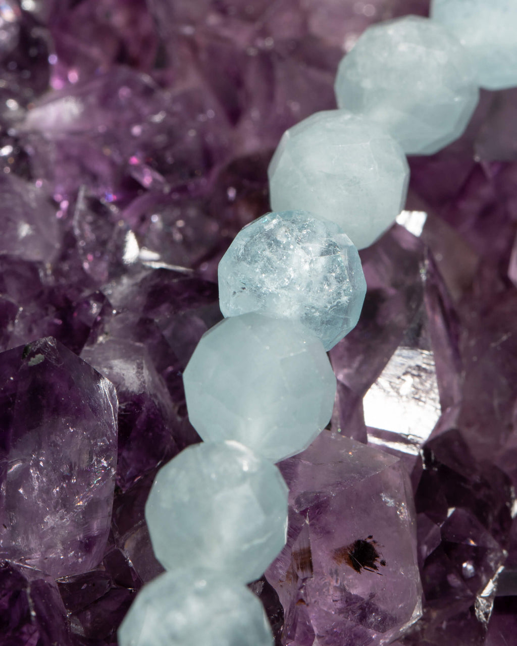 Detalle macro de las cuentas facetadas de Aguamarina con su transparencia, sobre amatista