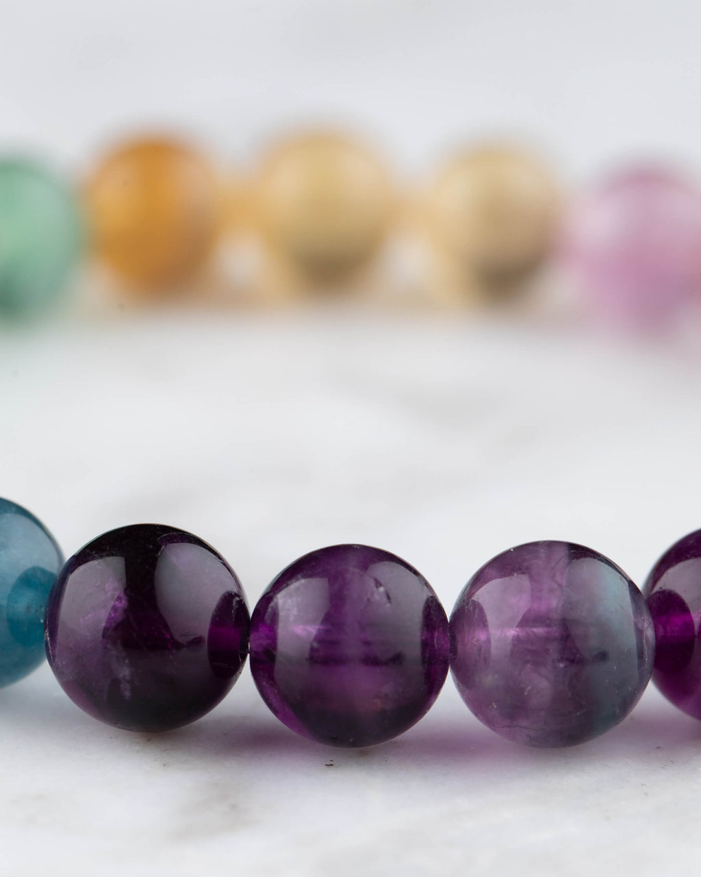 Pulsera de Fluorita Arcoiris vista en angulo, morado en primer plano y degradado de fondo
