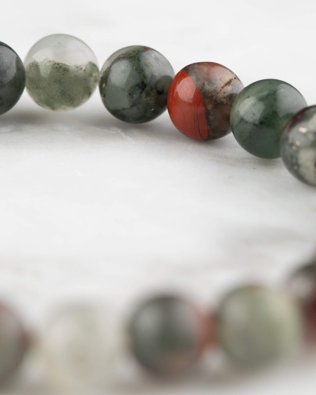 Detalle de las cuentas de Piedra Sangre en curva, con tonos verde oscuro, gris y rojo
