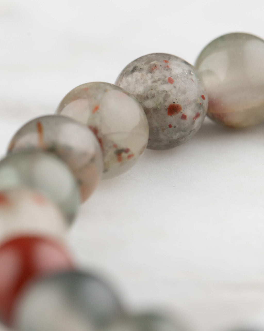 Acercamiento a las cuentas de Piedra Sangre de la pulsera, enfoque en el moteado rojo sobre gris