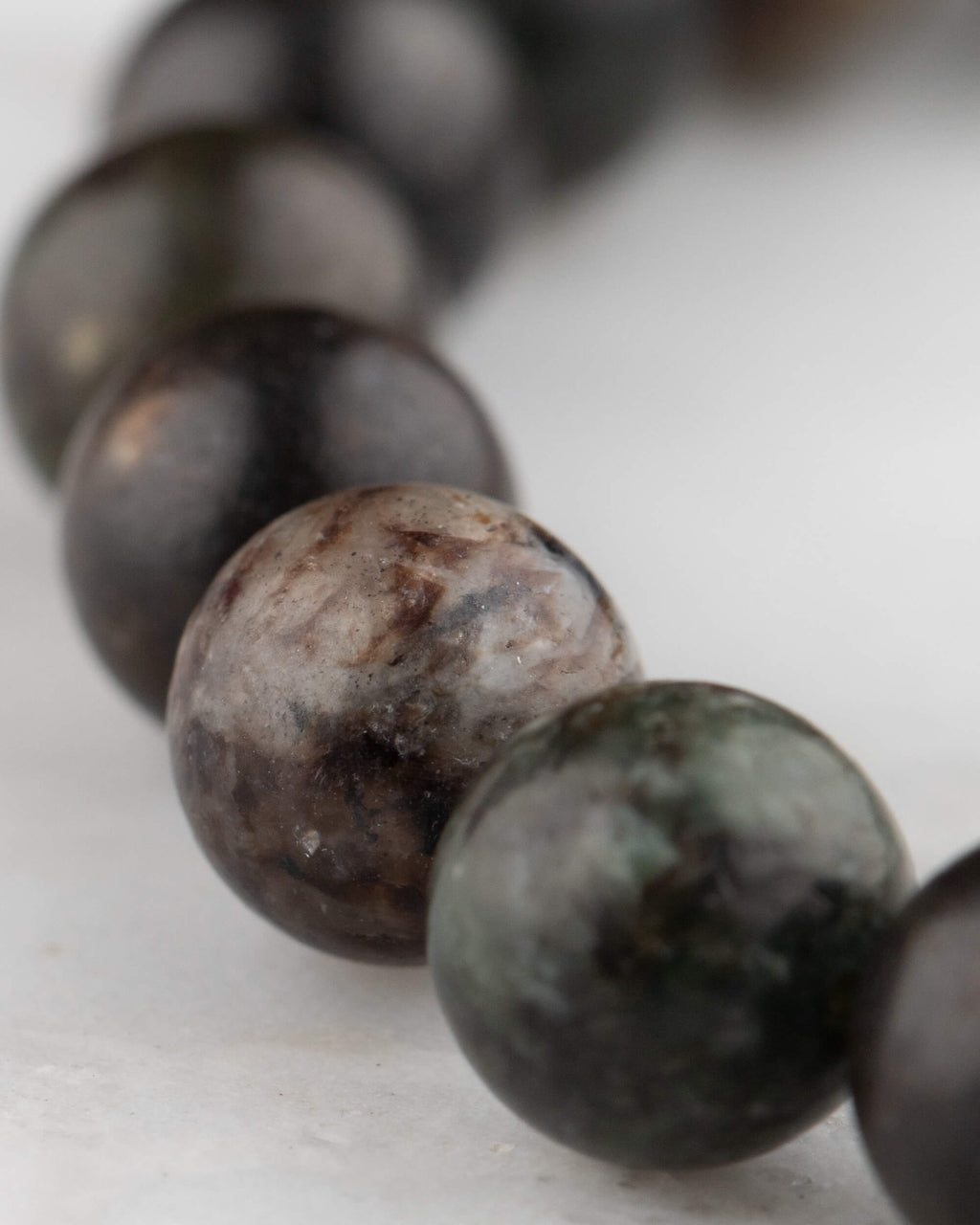 Detalle macro de las cuentas de Flogopita en tonos negro, gris y marrón sobre mármol claro