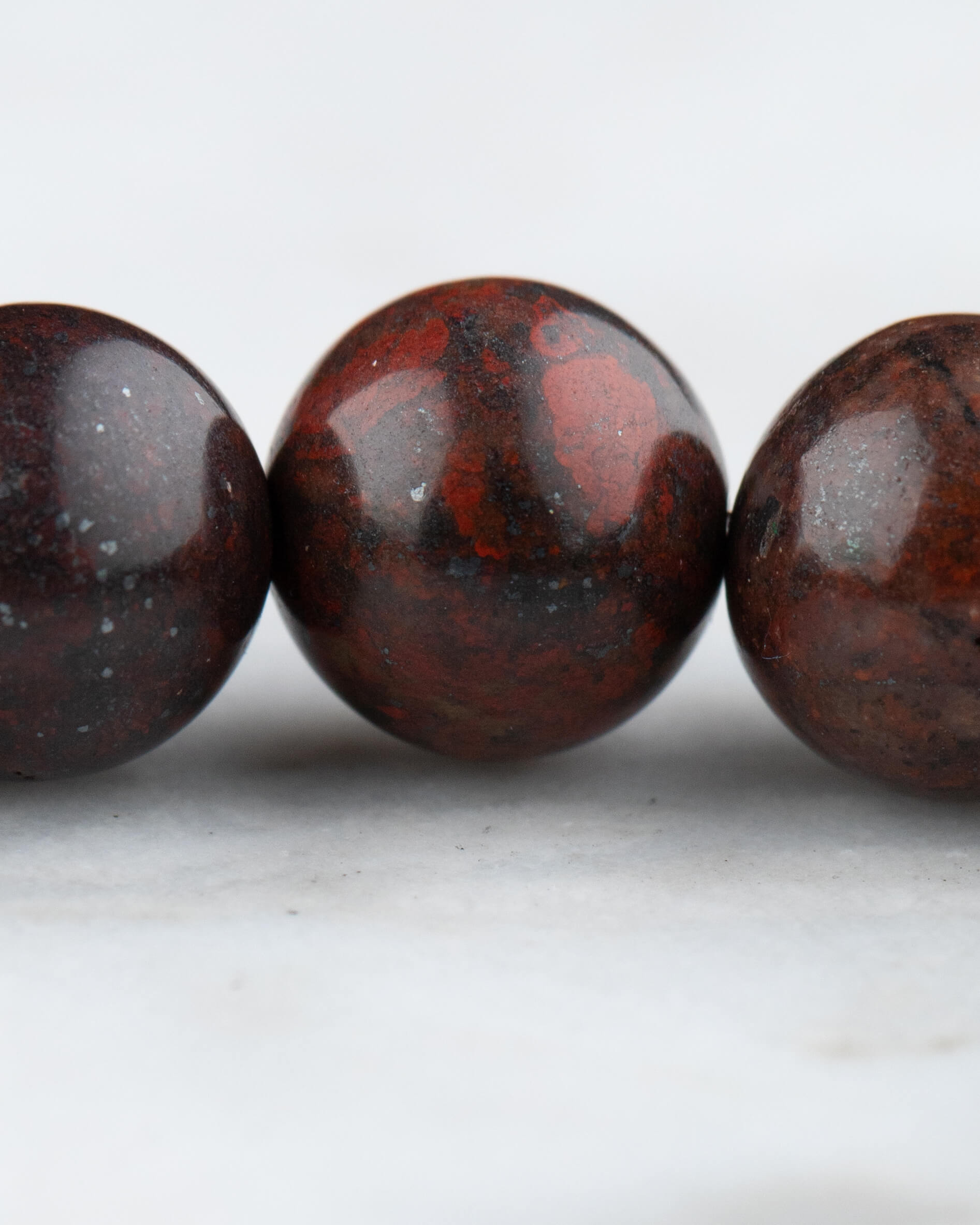 Detalle macro de tres cuentas de Jaspe Rojo Oscuro con vetas rojizas y negras