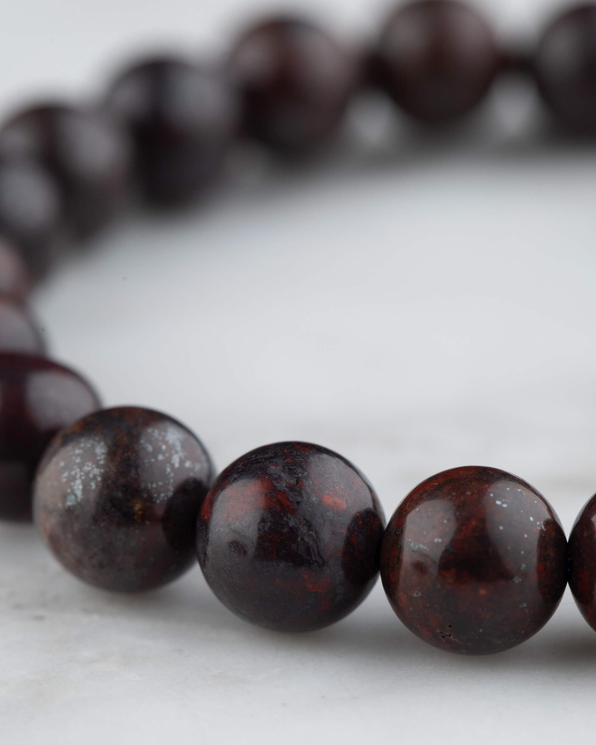 Detalle cercano de la pulsera de Jaspe Rojo Oscuro sobre superficie de mármol