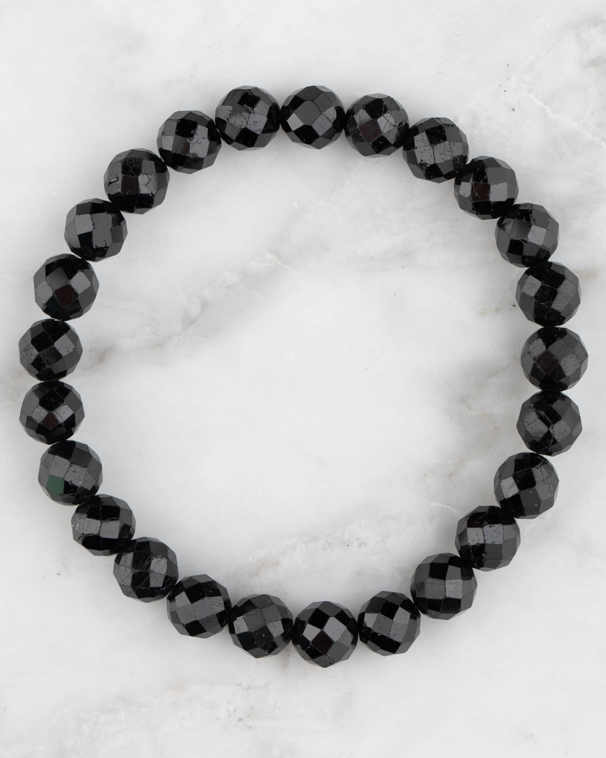Pulsera de Turmalina Negra facetada de 8 mm, pieza completa en círculo sobre mármol