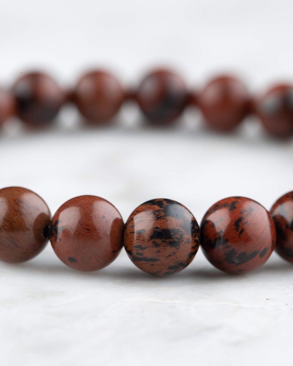 Cuentas de Obsidiana Caoba en detalle cercano, arco de la pulsera sobre superficie clara