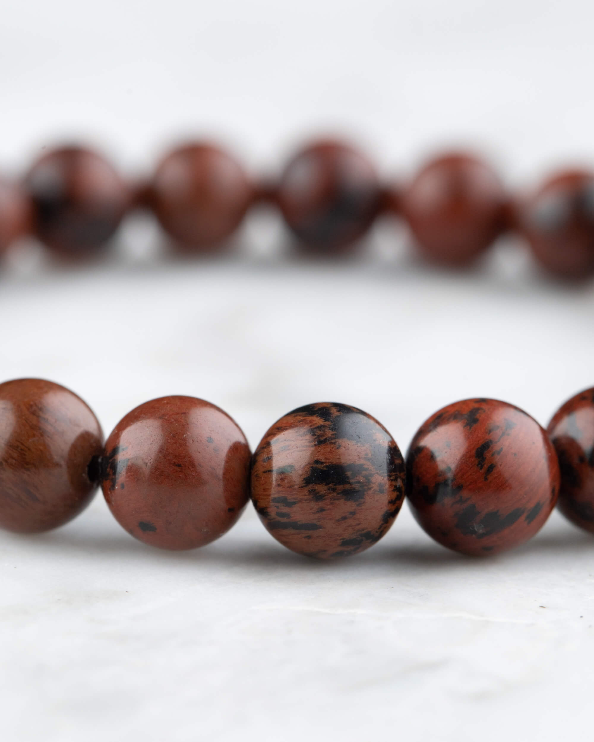 Cuentas de Obsidiana Caoba en detalle cercano, arco de la pulsera sobre superficie clara