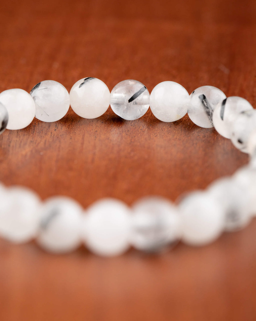 Pulsera de Cuarzo Turmalinado en curva mostrando hilos negros de turmalina sobre madera
