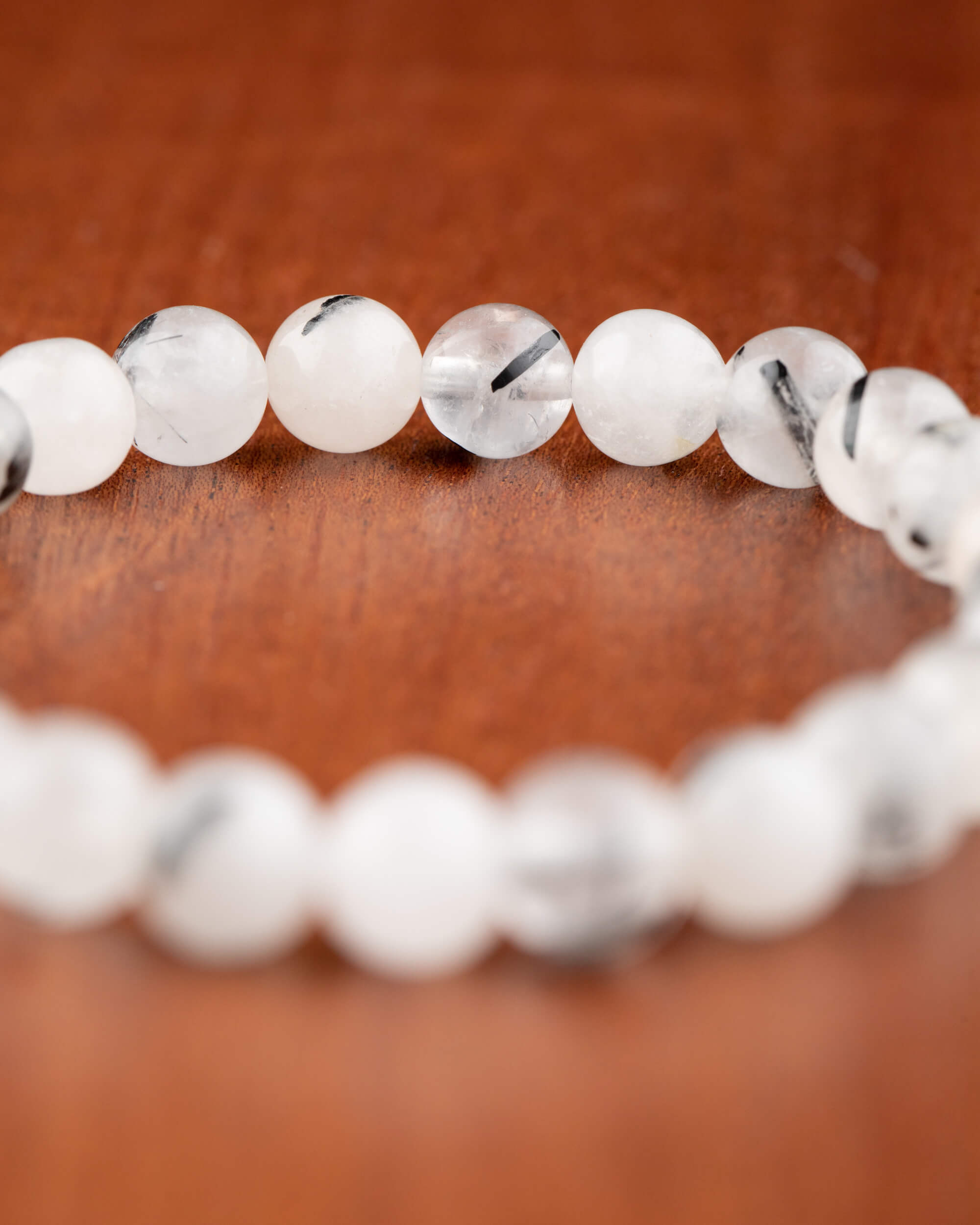 Pulsera de Cuarzo Turmalinado en curva mostrando hilos negros de turmalina sobre madera