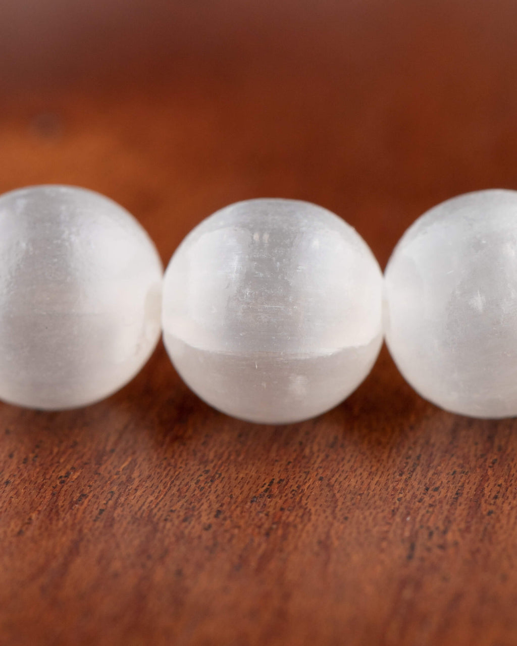 Detalle macro de tres cuentas de Selenita en primer plano sobre madera