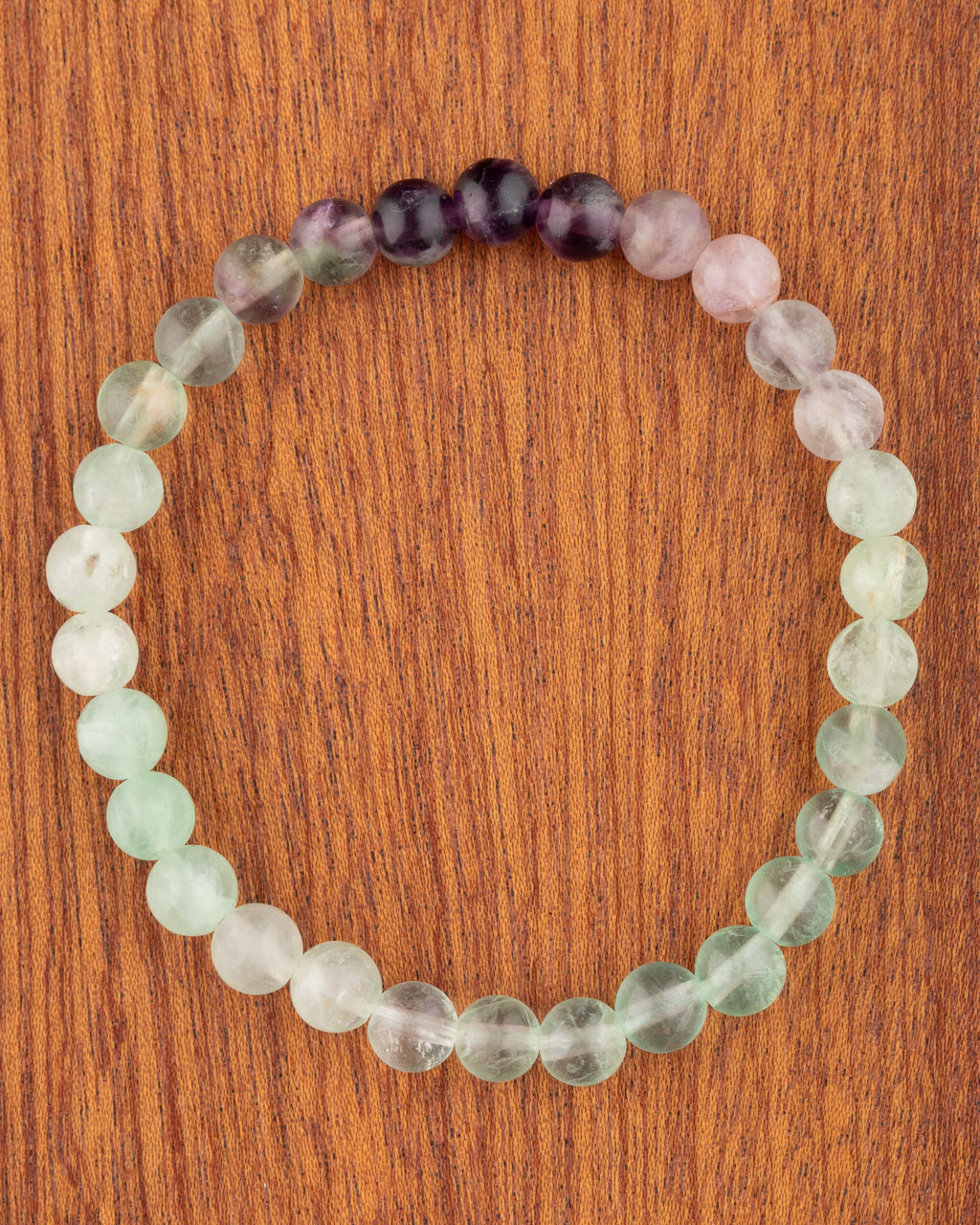Pulsera de Fluorita de 6 mm, pieza completa en círculo con tonos verde, lila y morado sobre madera