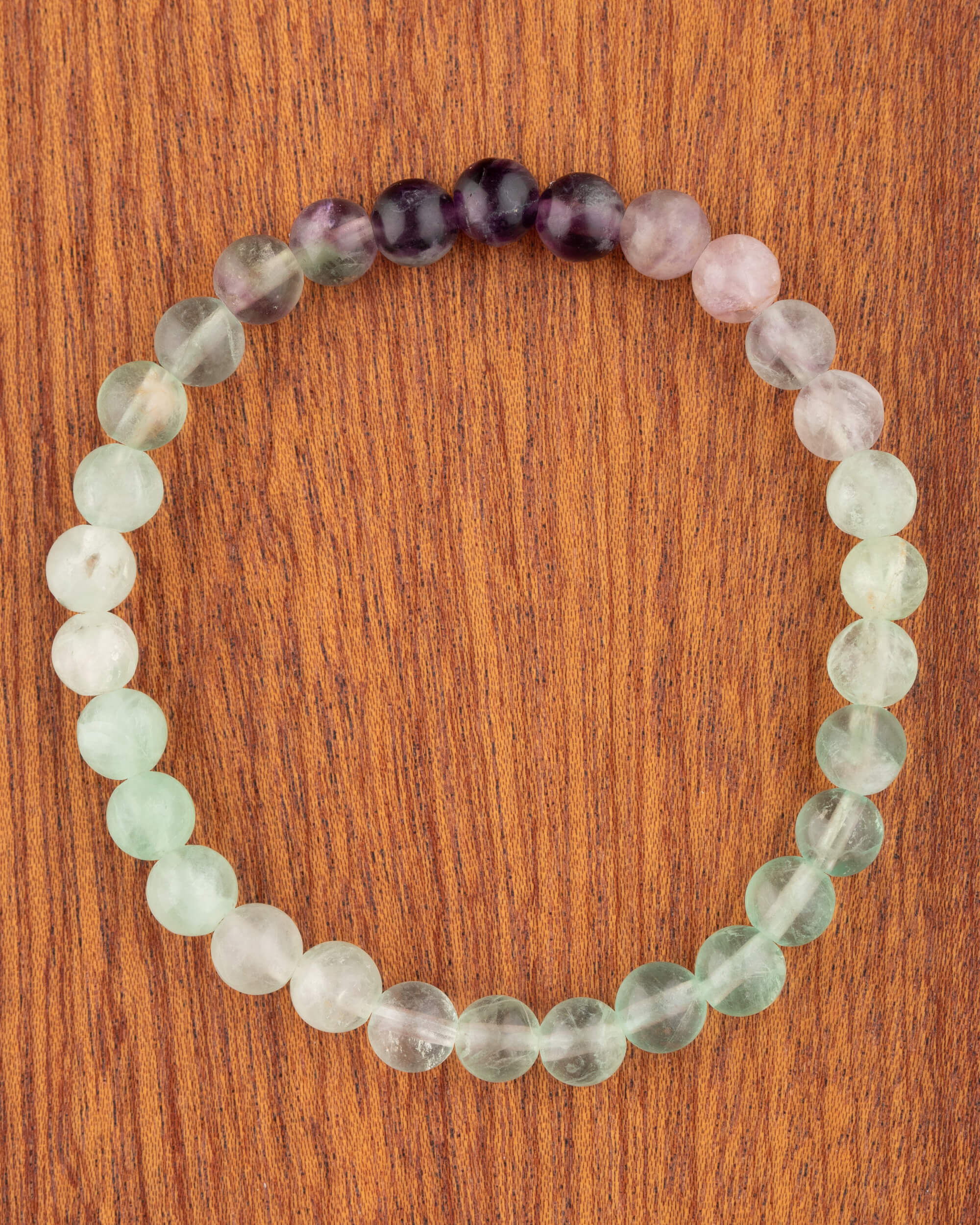 Pulsera de Fluorita de 6 mm, pieza completa en círculo con tonos verde, lila y morado sobre madera