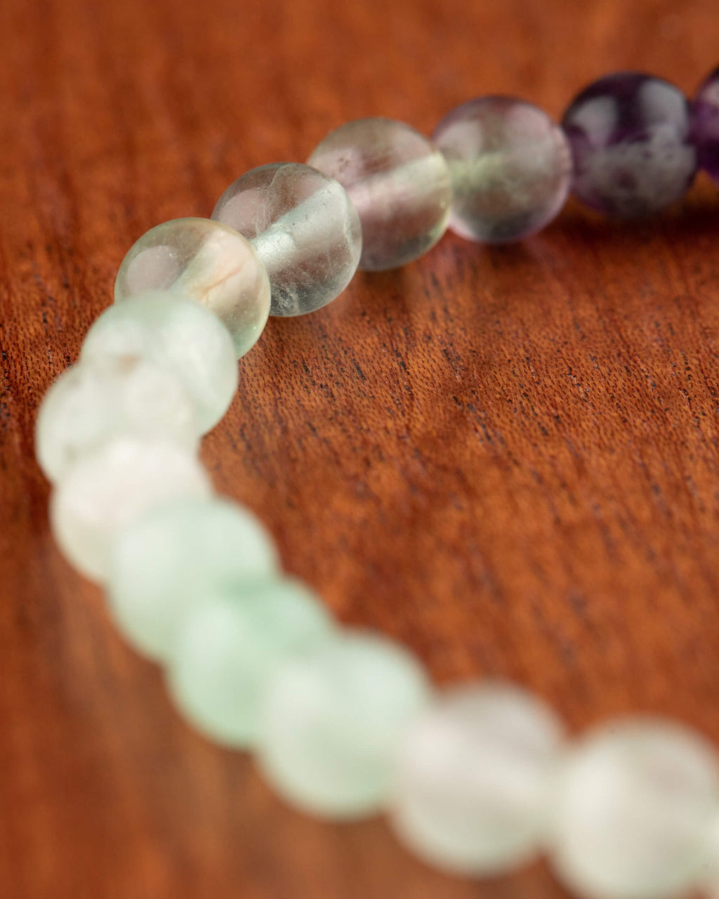 Pulsera de Fluorita vista en curva, cuentas moradas y verdes con degradado de enfoque