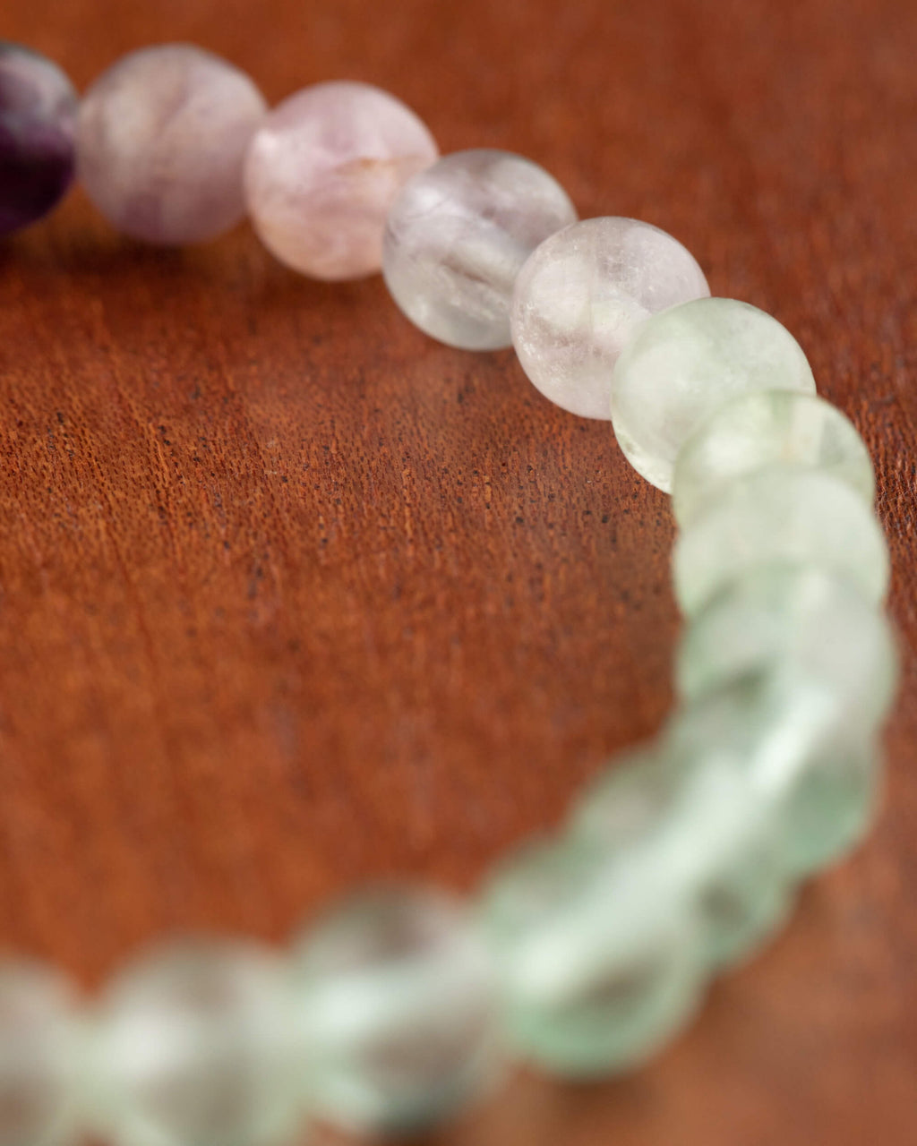 Pulsera de Fluorita en ángulo, transición de cuentas lilas a verdes sobre superficie de madera