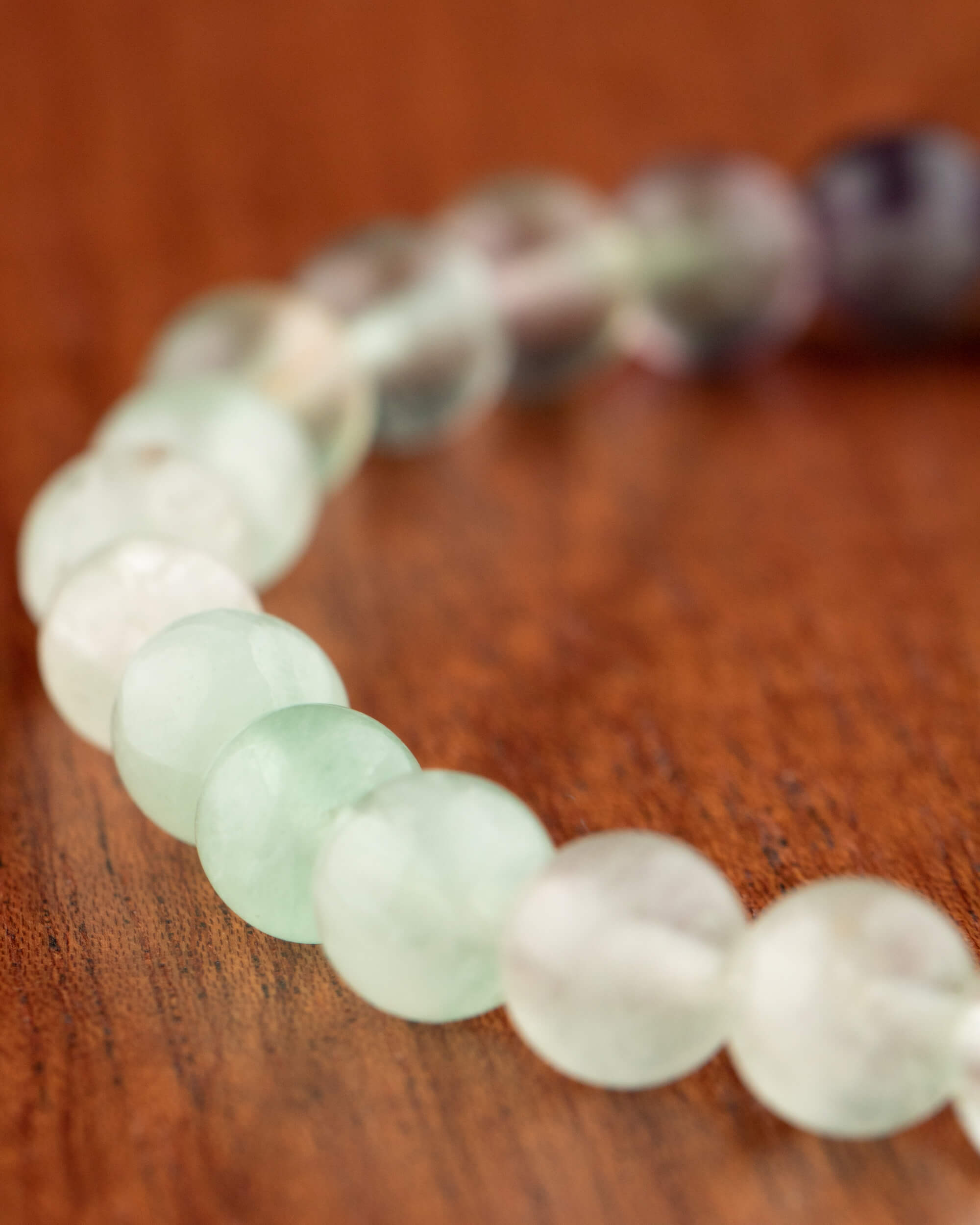 Pulsera de Fluorita en ángulo, cuentas verdes en primer plano y tonos morados difuminados al fondo