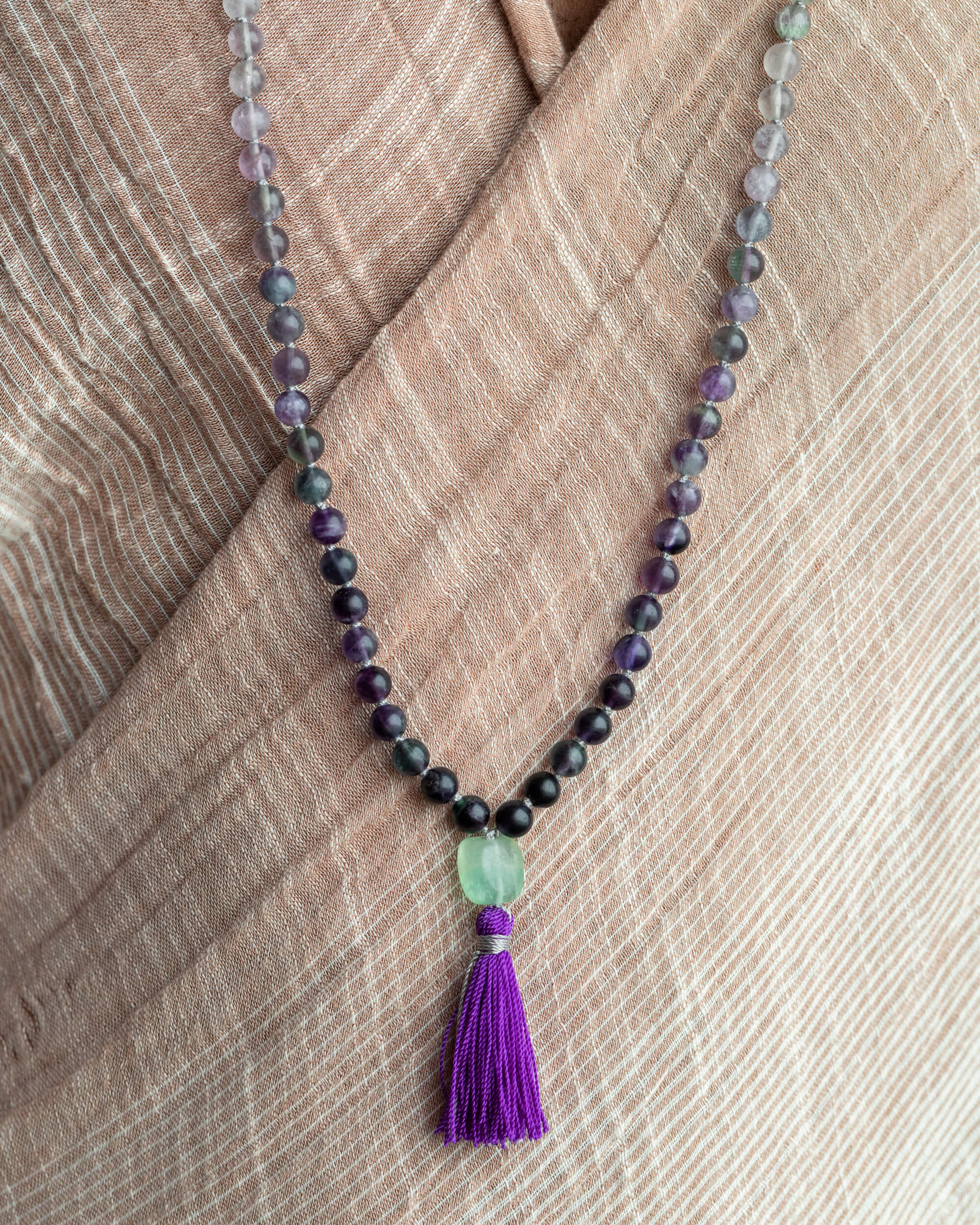 Japa Mala de Fluorita con borla morada cayendo sobre tela clara