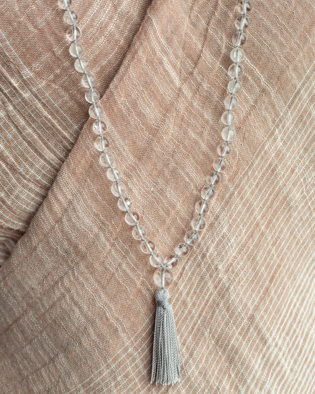 Japa Mala de Cuarzo Transparente con borla gris cayendo sobre tela