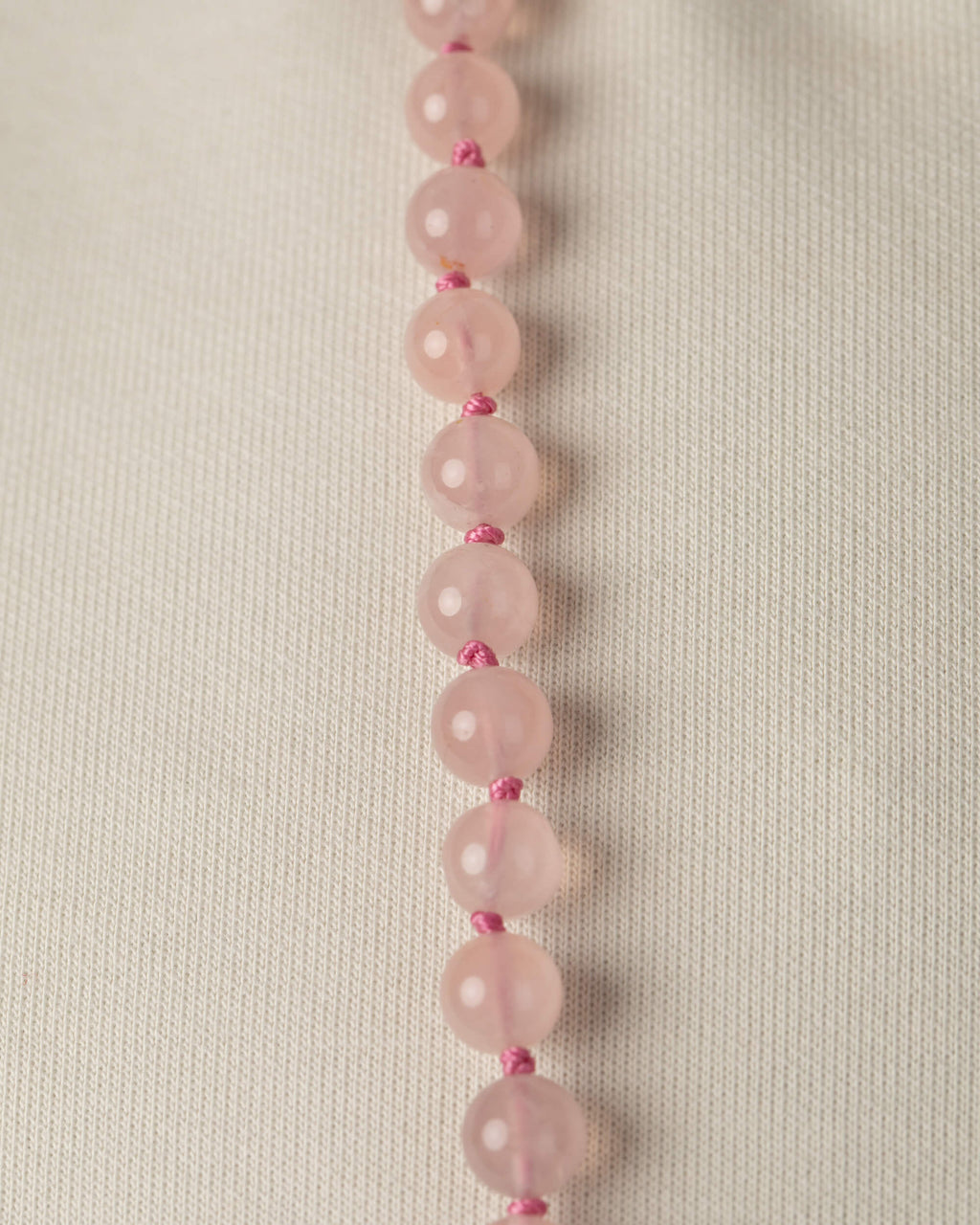 Detalle macro vertical de las cuentas de Cuarzo Rosa sobre tela clara