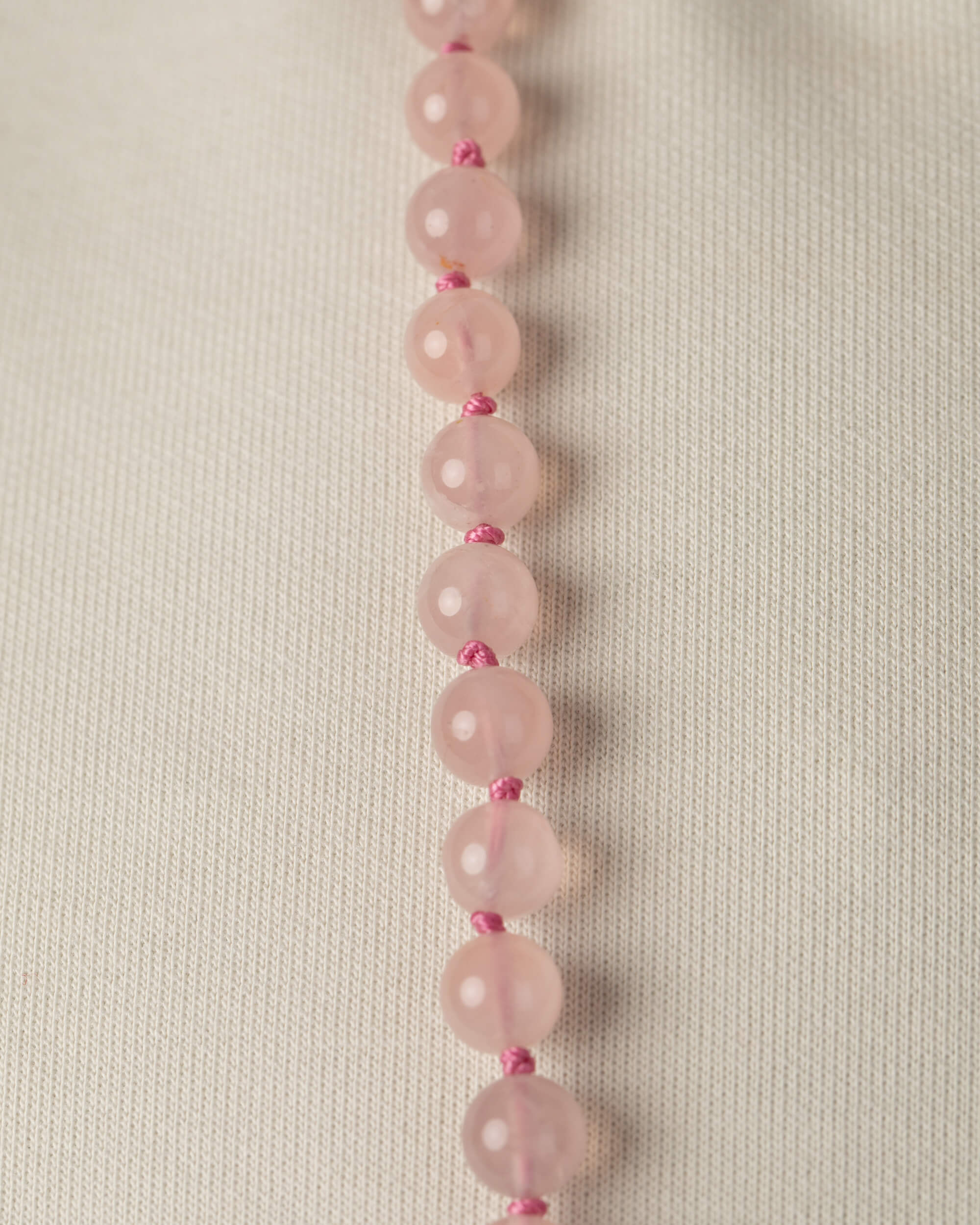 Detalle macro vertical de las cuentas de Cuarzo Rosa sobre tela clara