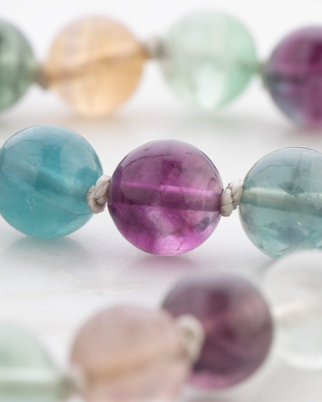 Detalle macro de las cuentas de Fluorita Arcoíris en tonos morado, azul y ámbar