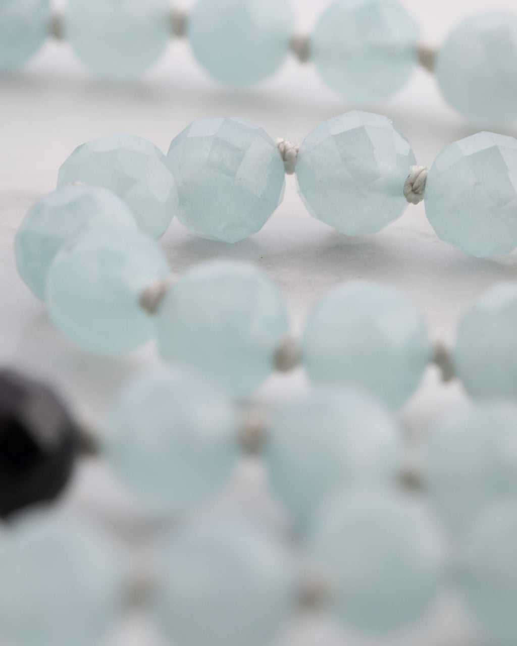 Detalle macro de las cuentas facetadas de Aguamarina, luz suave sobre mármol