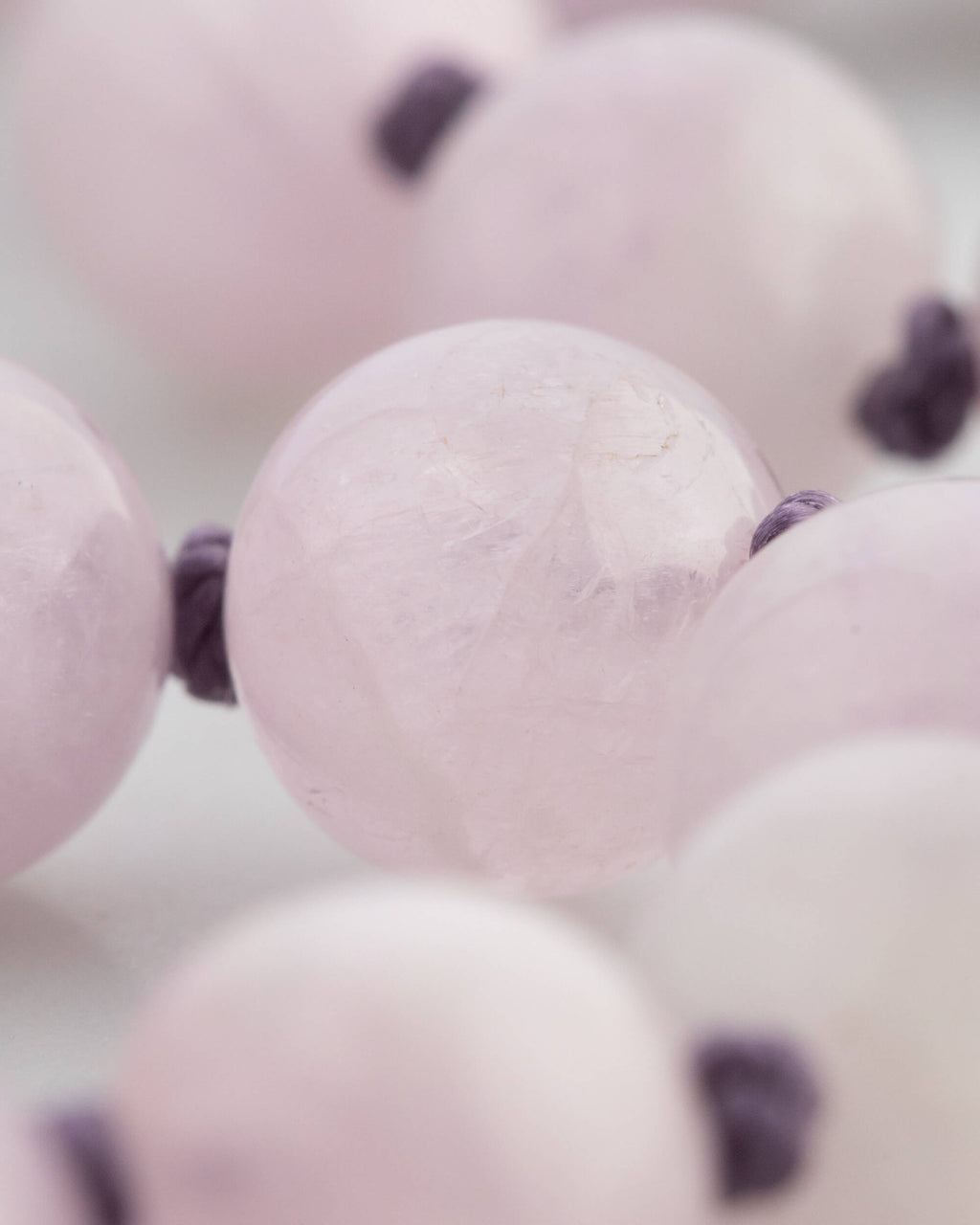 Detalle macro de una cuenta de Kunzita con nudo de hilo violeta