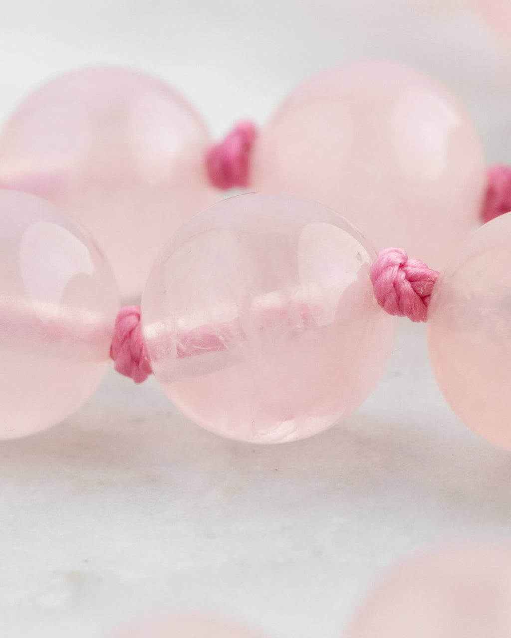 Detalle macro de las cuentas translúcidas de Cuarzo Rosa con nudo fucsia