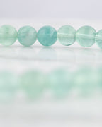 Detalle macro de las cuentas translúcidas verde agua de Fluorita sobre superficie clara