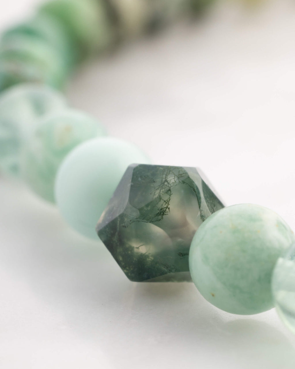 Detalle macro de cuenta facetada verde con vetas blancas tipo musgo junto a cuentas verde claro del Codificador Corazon