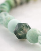 Detalle macro de cuenta facetada verde con vetas blancas tipo musgo junto a cuentas verde claro del Codificador Corazon