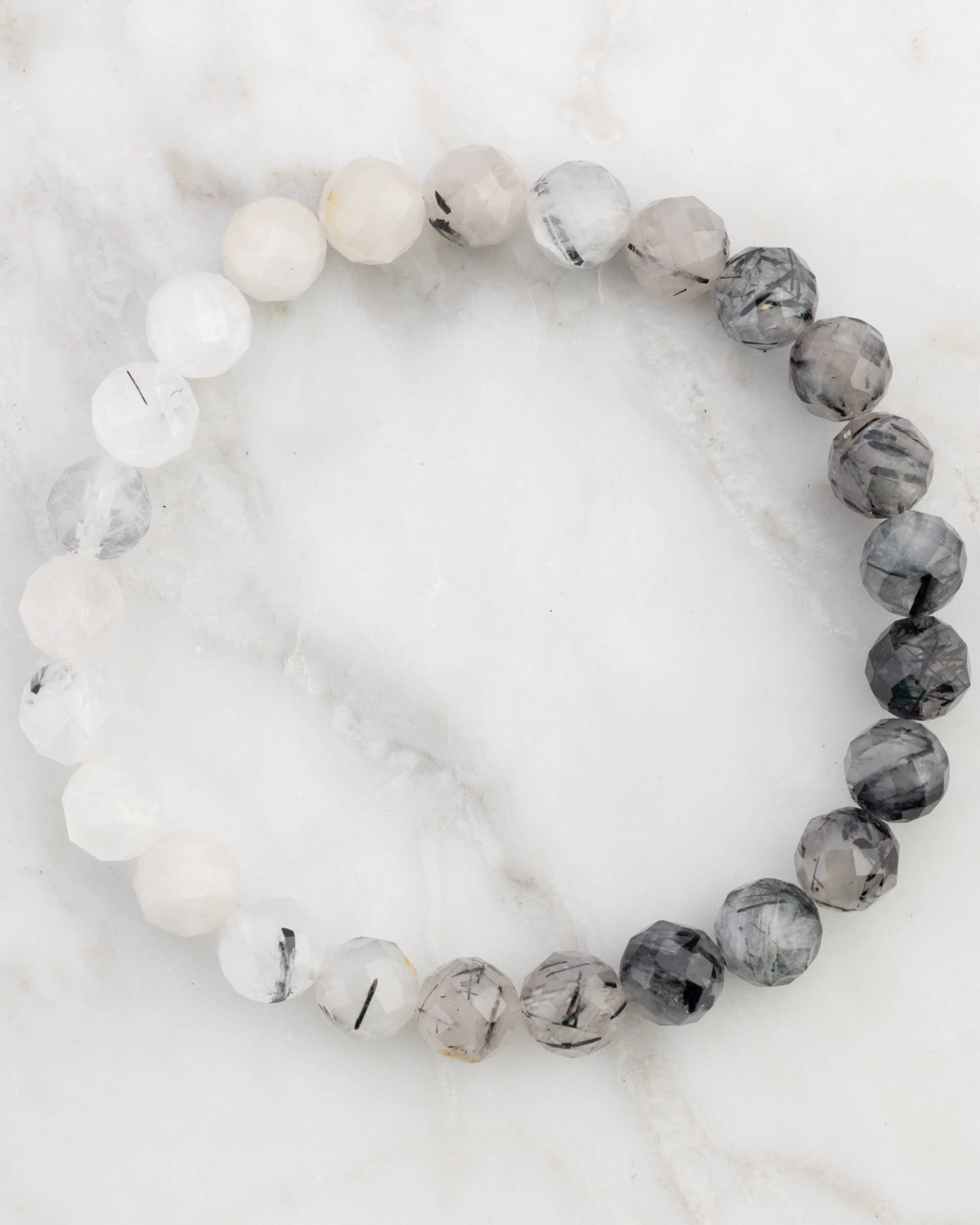 Pulsera de Cuarzo Turmalinado facetada de 8 mm, pieza completa en círculo sobre mármol claro