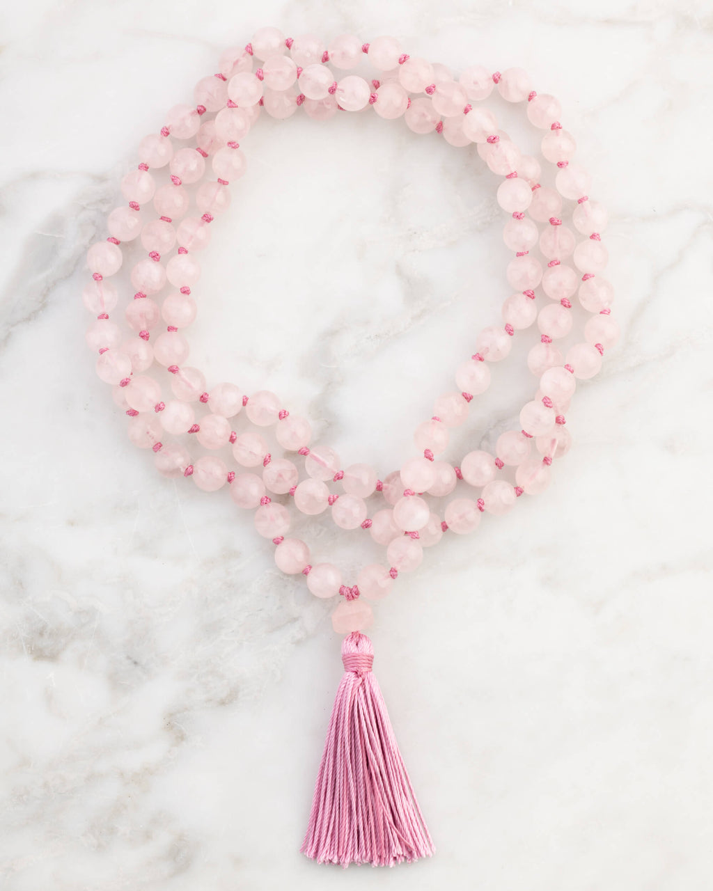 Japa Mala de Cuarzo Rosa enrollado, pieza completa con borlón rosa sobre mármol