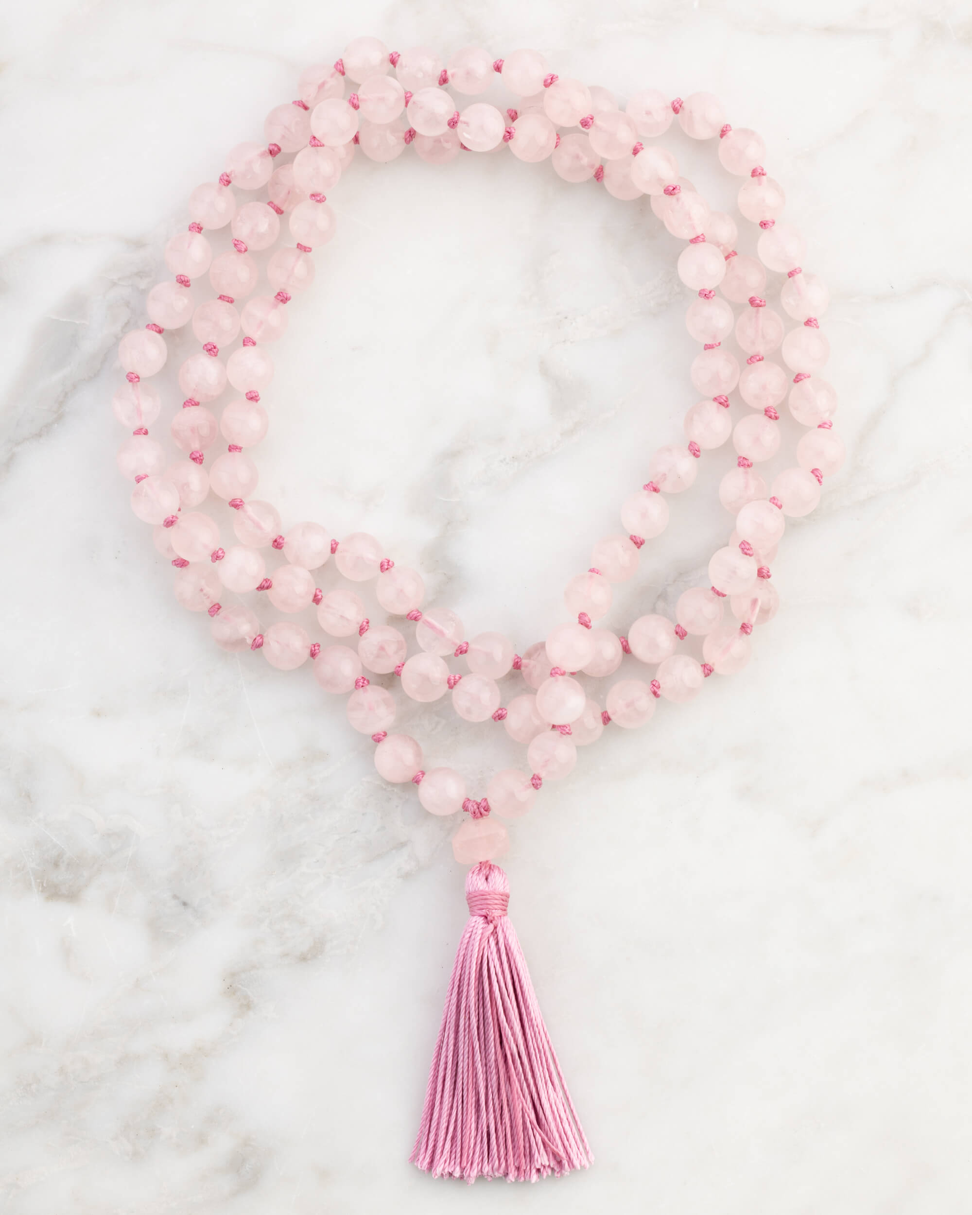 Japa Mala de Cuarzo Rosa enrollado, pieza completa con borlón rosa sobre mármol