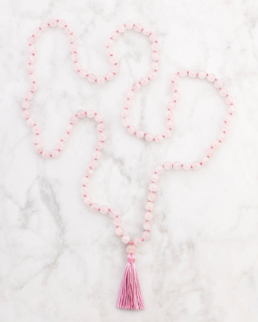 Japa Mala de Cuarzo Rosa extendido en forma de S sobre superficie de mármol