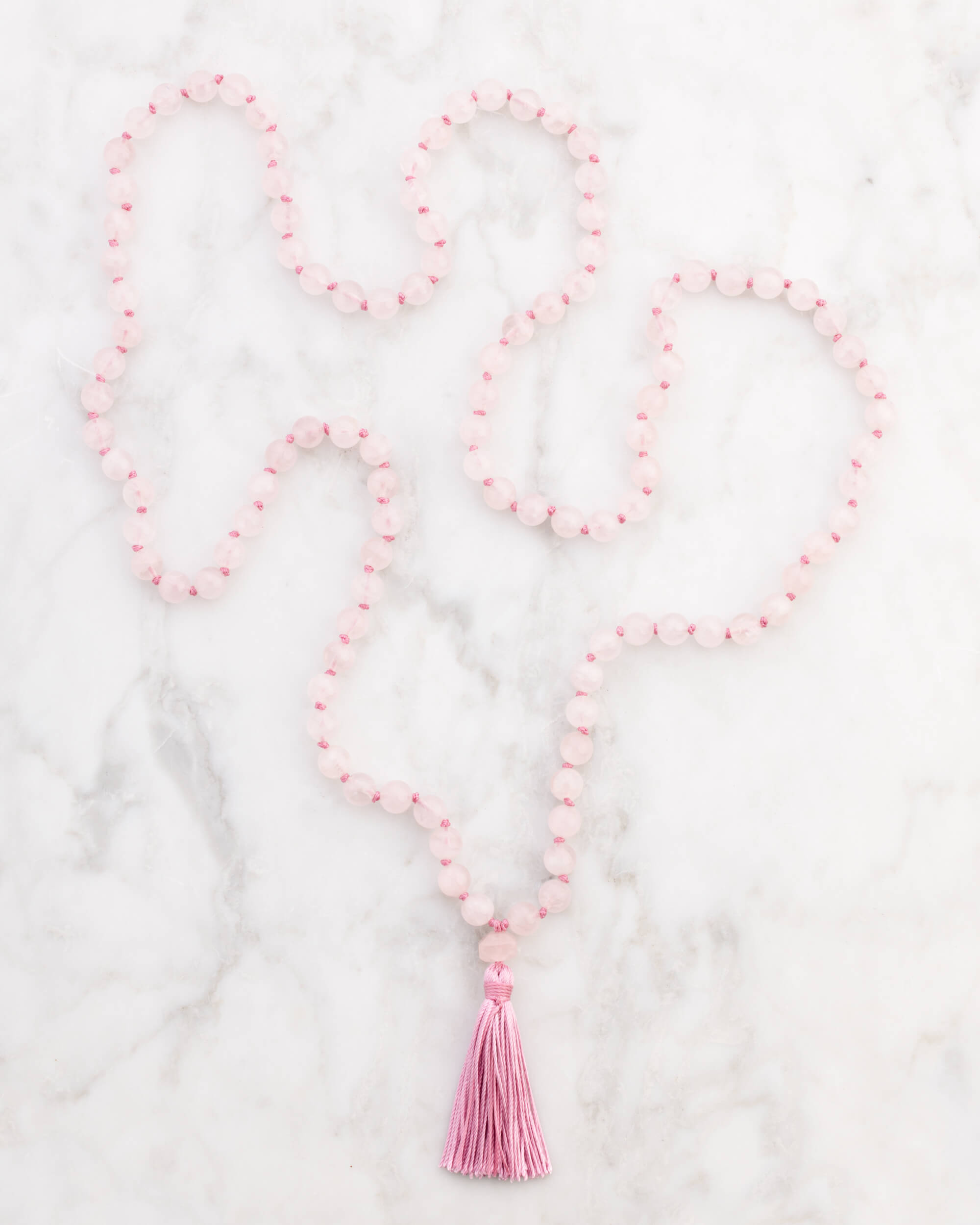 Japa Mala de Cuarzo Rosa extendido en forma de S sobre superficie de mármol