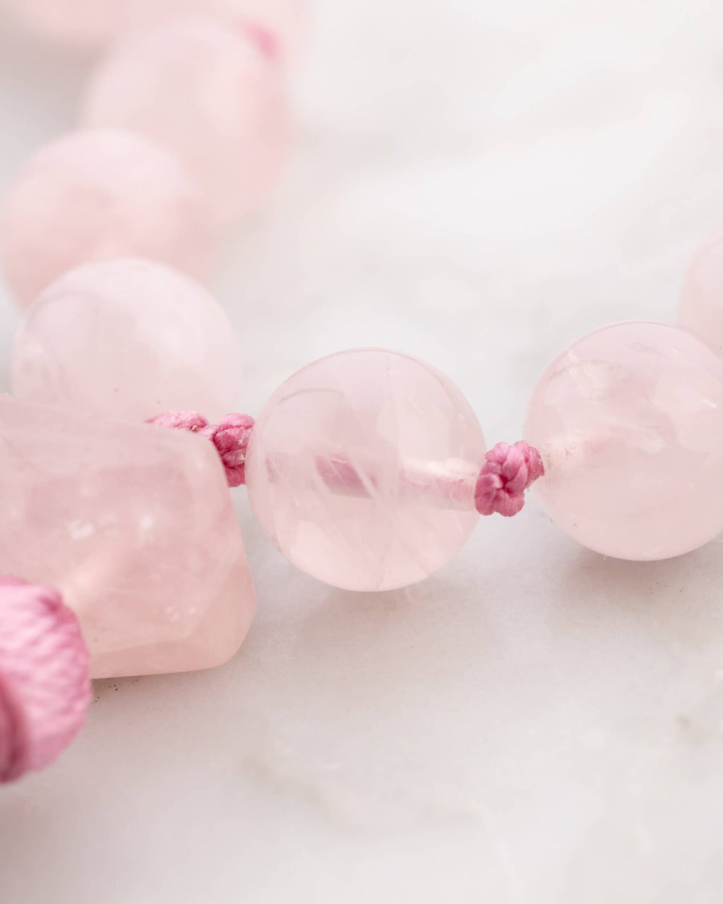 Detalle macro de las cuentas de Cuarzo Rosa sobre superficie de mármol