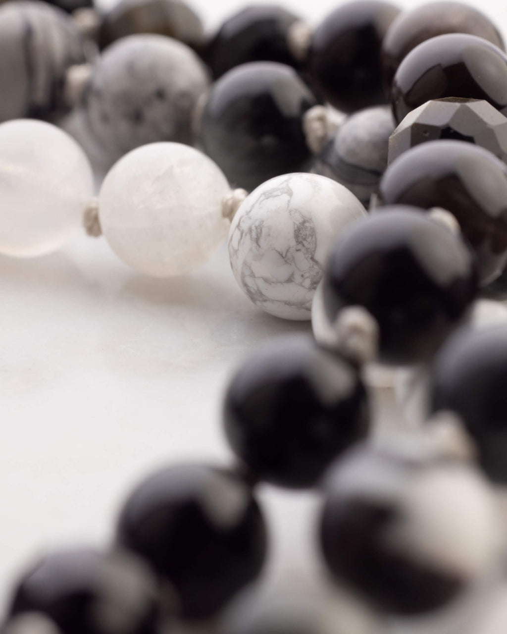 Detalle macro de una cuenta facetada gris opaca junto a cuentas blancas y negras