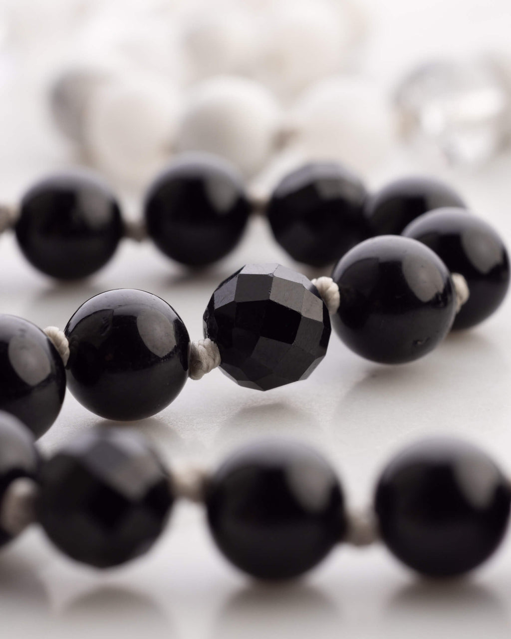 Detalle macro de una cuenta facetada de Obsidiana Negra entre cuentas lisas