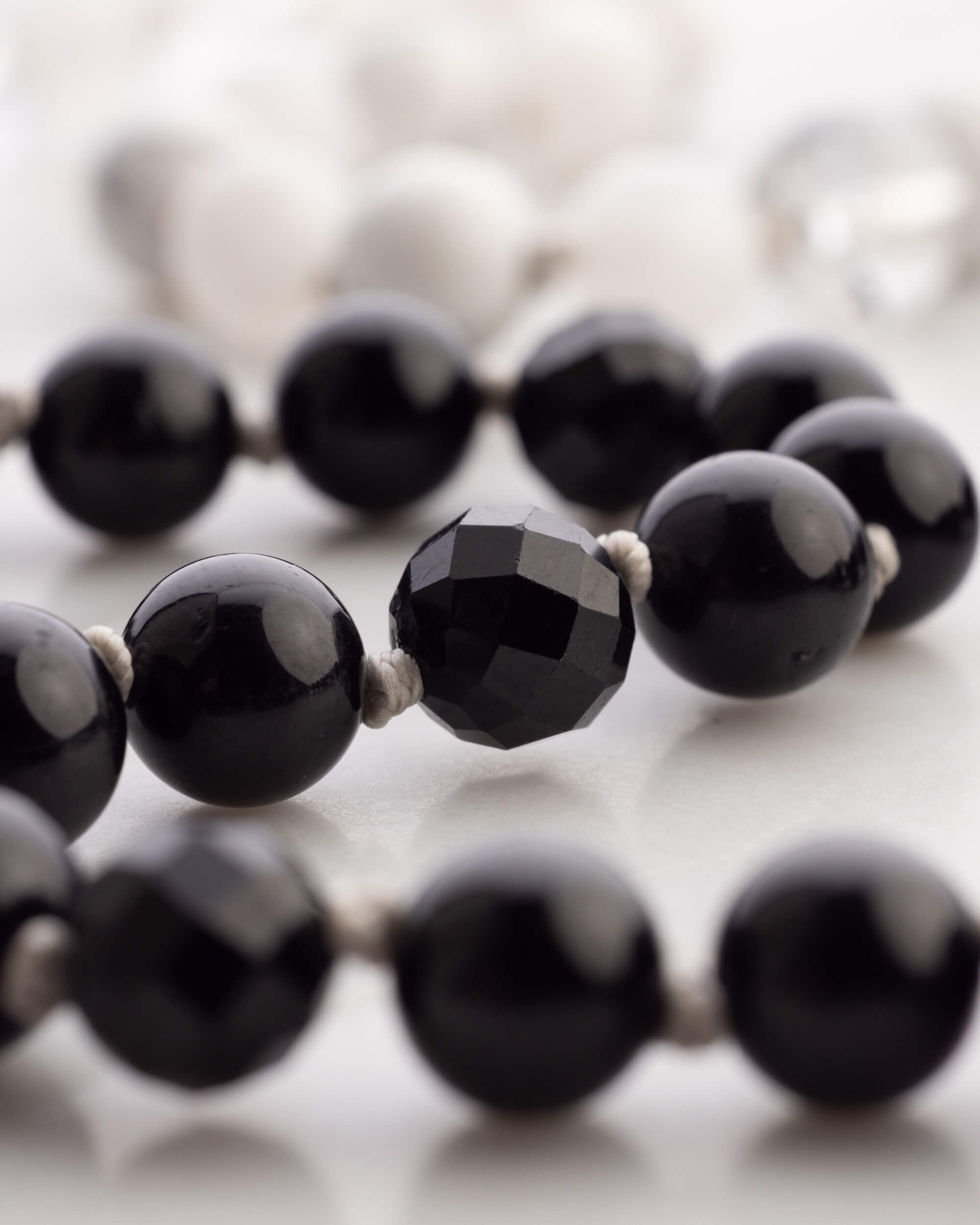 Detalle macro de una cuenta facetada de Obsidiana Negra entre cuentas lisas
