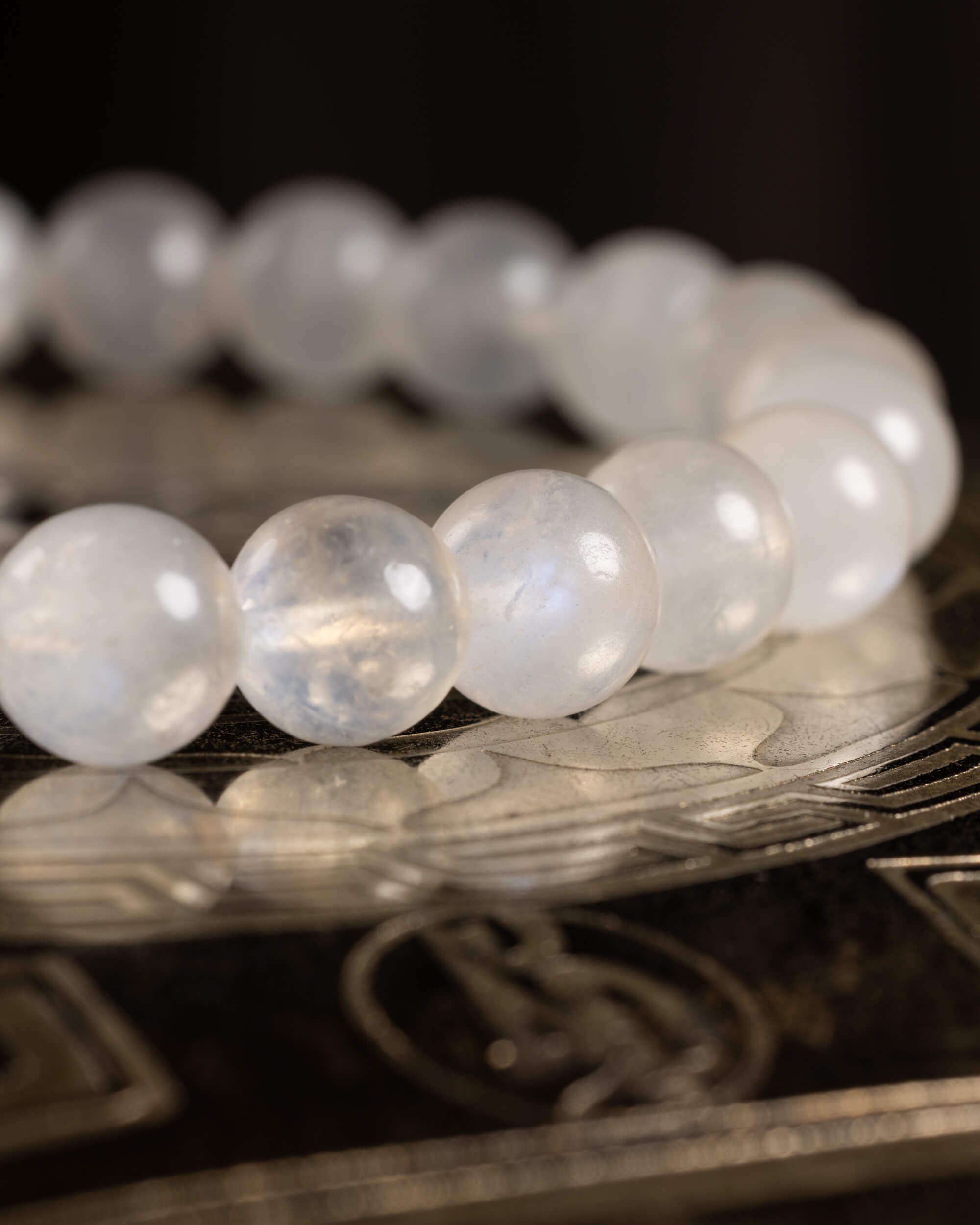 Pulsera de Piedra Luna desde ángulo bajo, curva de cuentas blancas sobre disco grabado