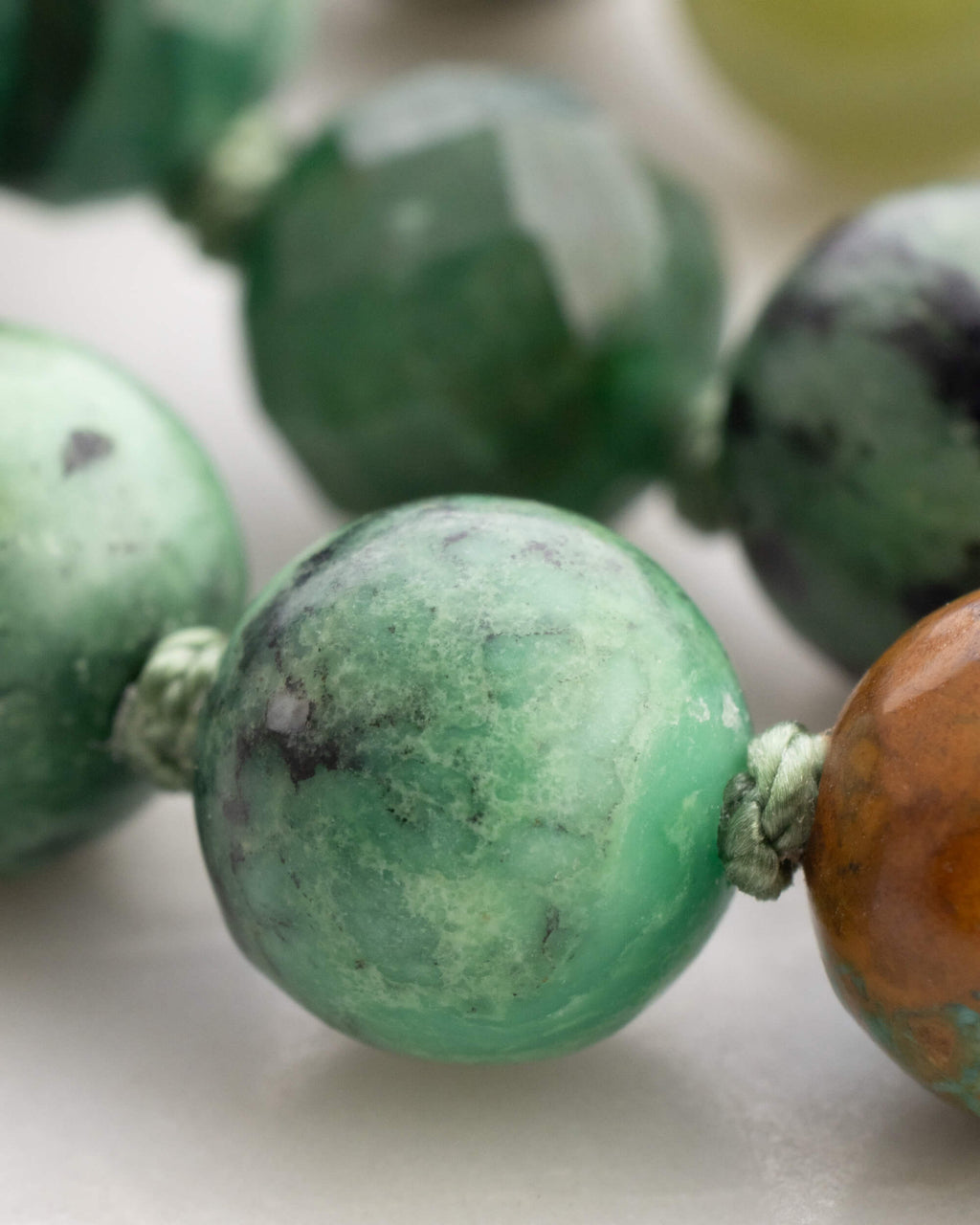 Detalle macro de cuentas facetadas verdes de Jade junto a una cuenta moteada verde y una ámbar del Japa Mala